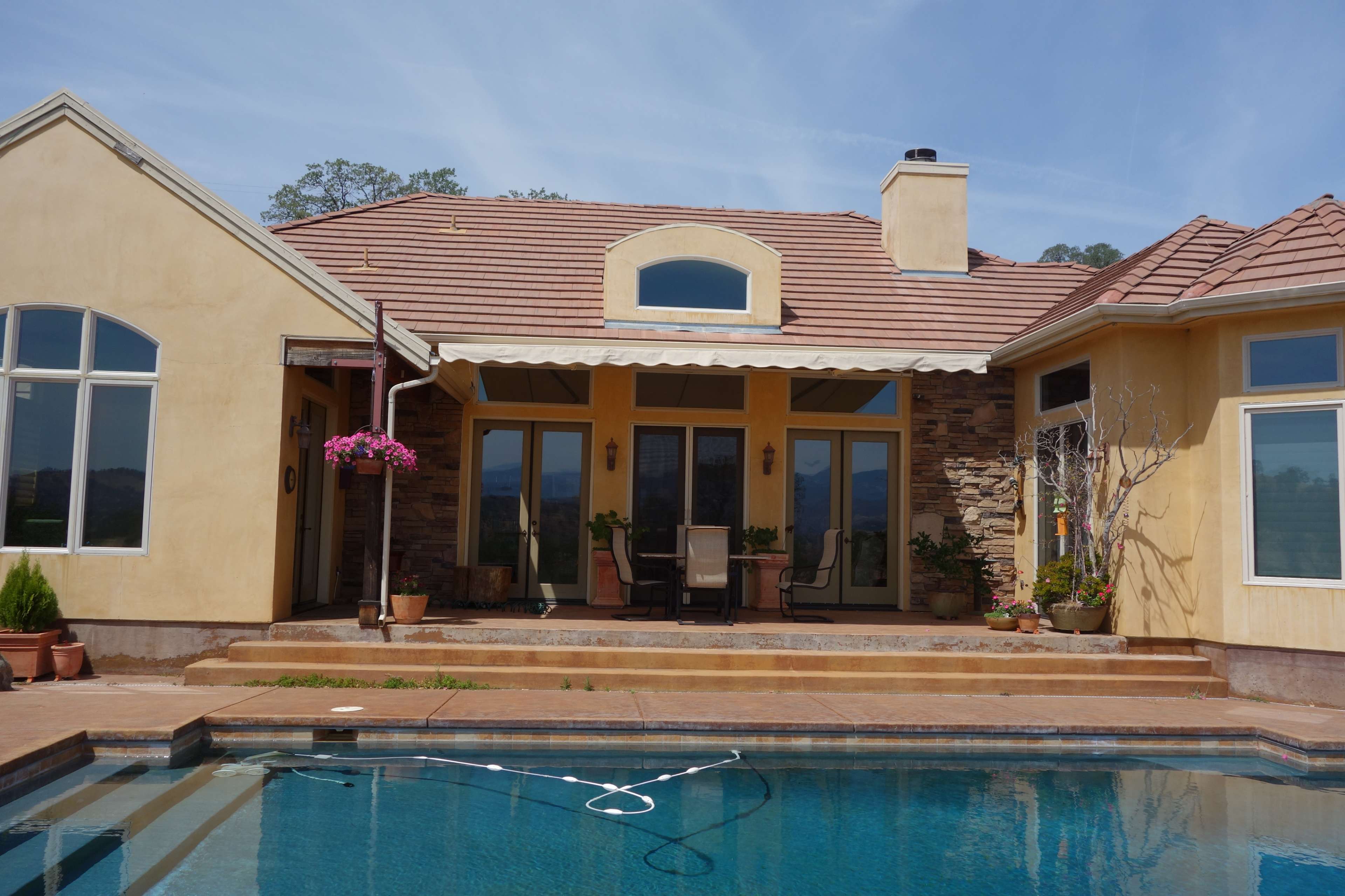 A villa-style home with a tan exterior, large windows, and a patio overlooking a swimming pool.