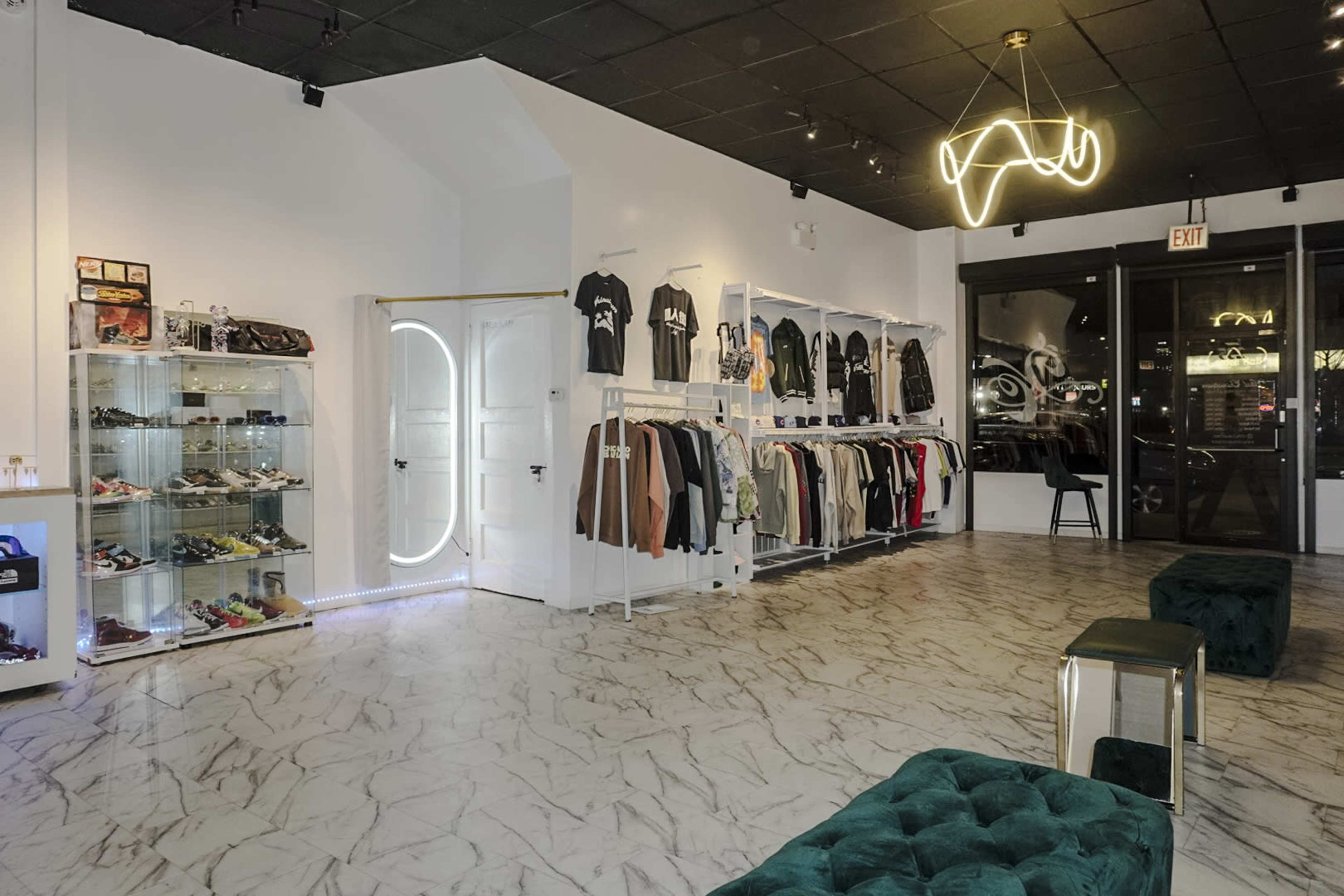 A modern retail space displaying clothing and shoes on shelves, with a mirrored door and a stylish light fixture overhead.