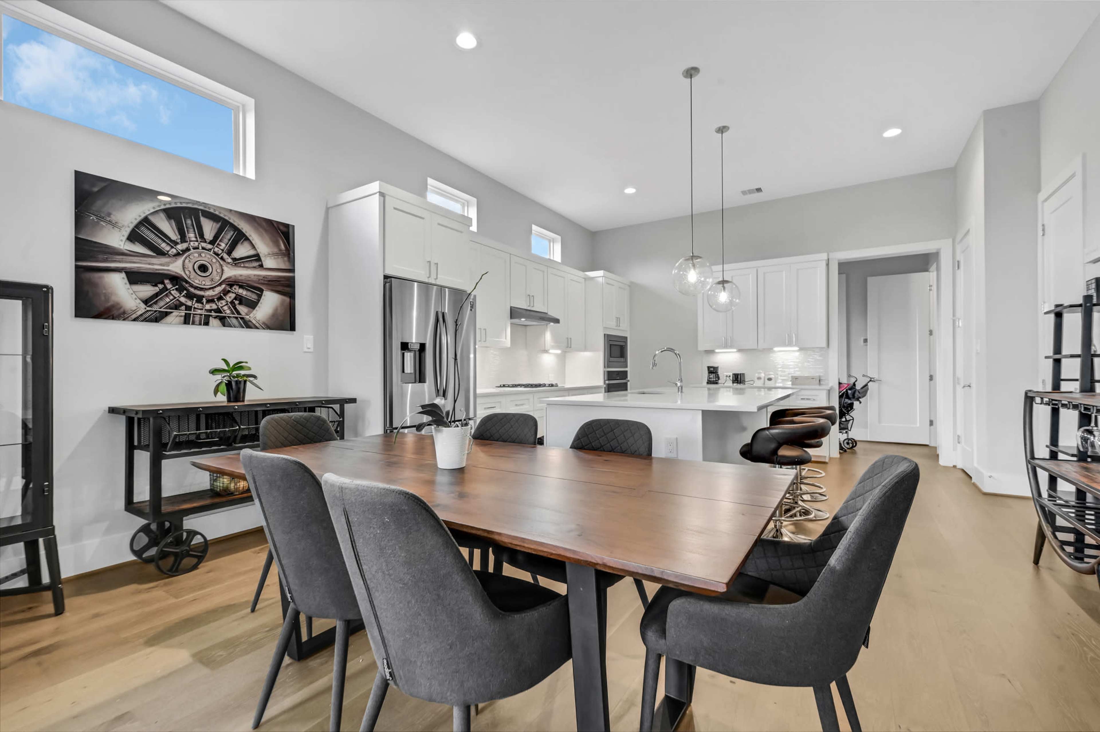 A modern dining area features a wooden table surrounded by black chairs, with a sleek kitchen visible in the background.