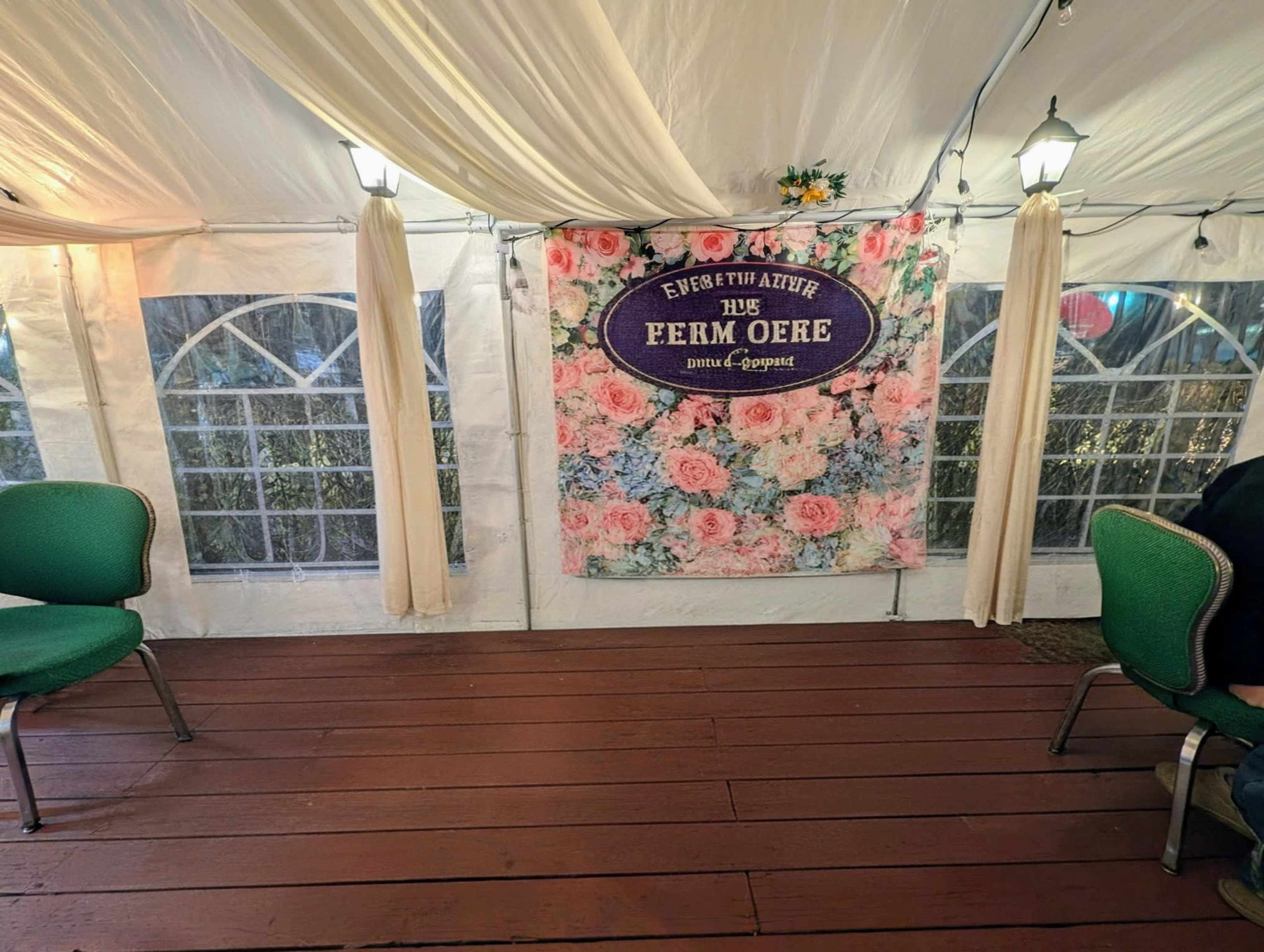 The image shows an interior of a decorated tent with a floral backdrop displaying the text "Everything the Ferm Oere" and green chairs arranged on a wooden floor.