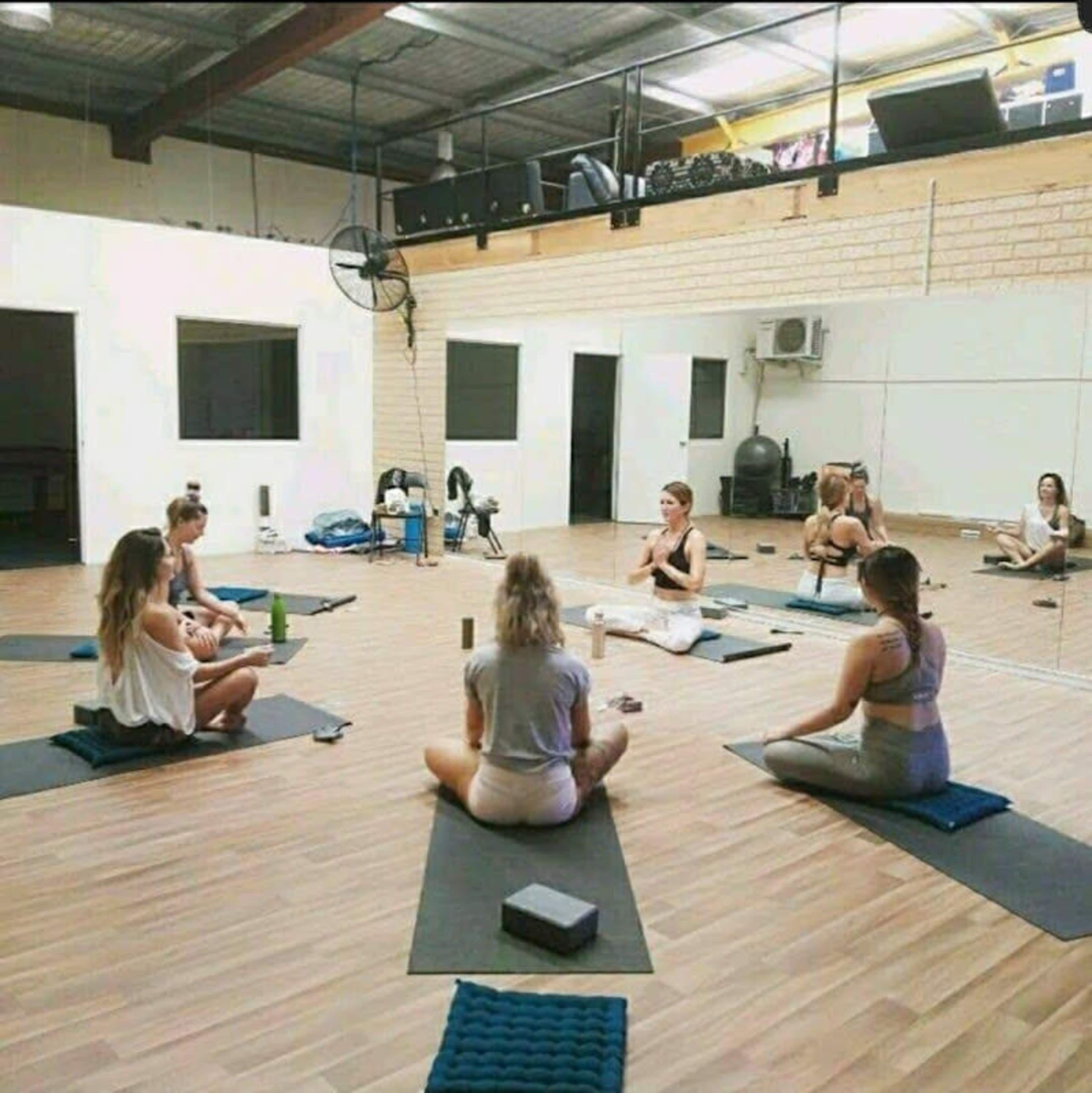 A group of women practice yoga on mats in a spacious, well-lit studio.