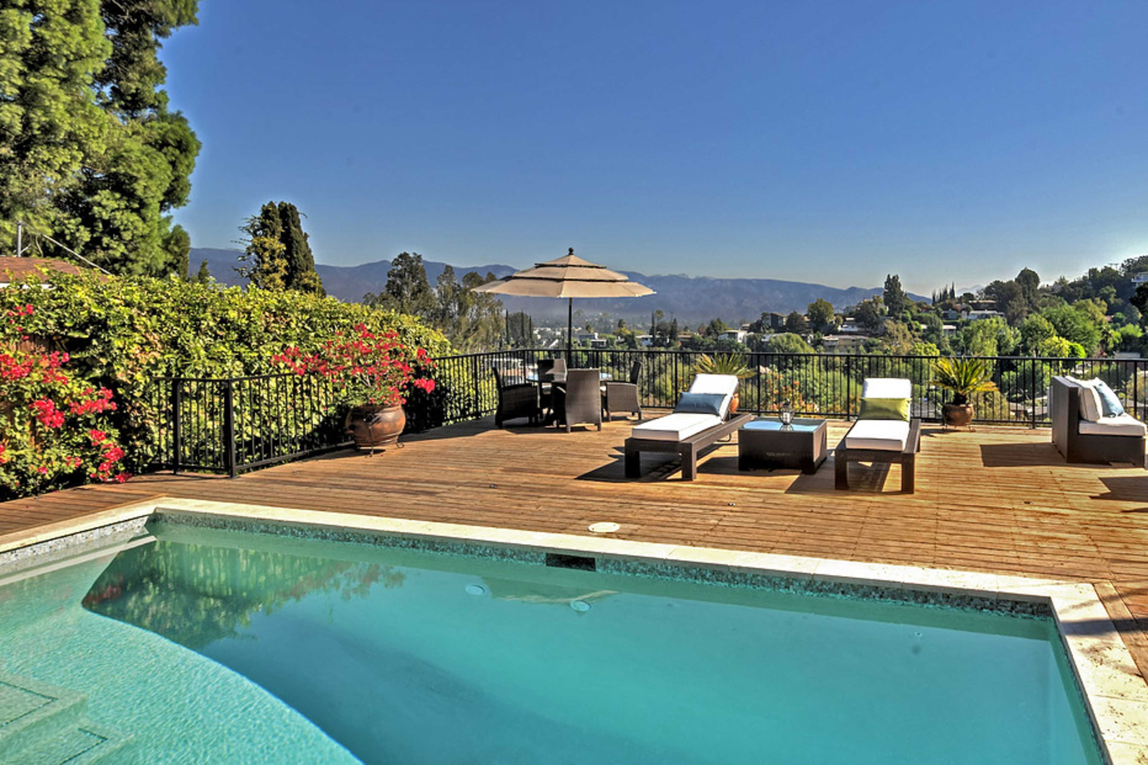 A swimming pool is situated on a wooden deck surrounded by lush greenery and a view of distant mountains.