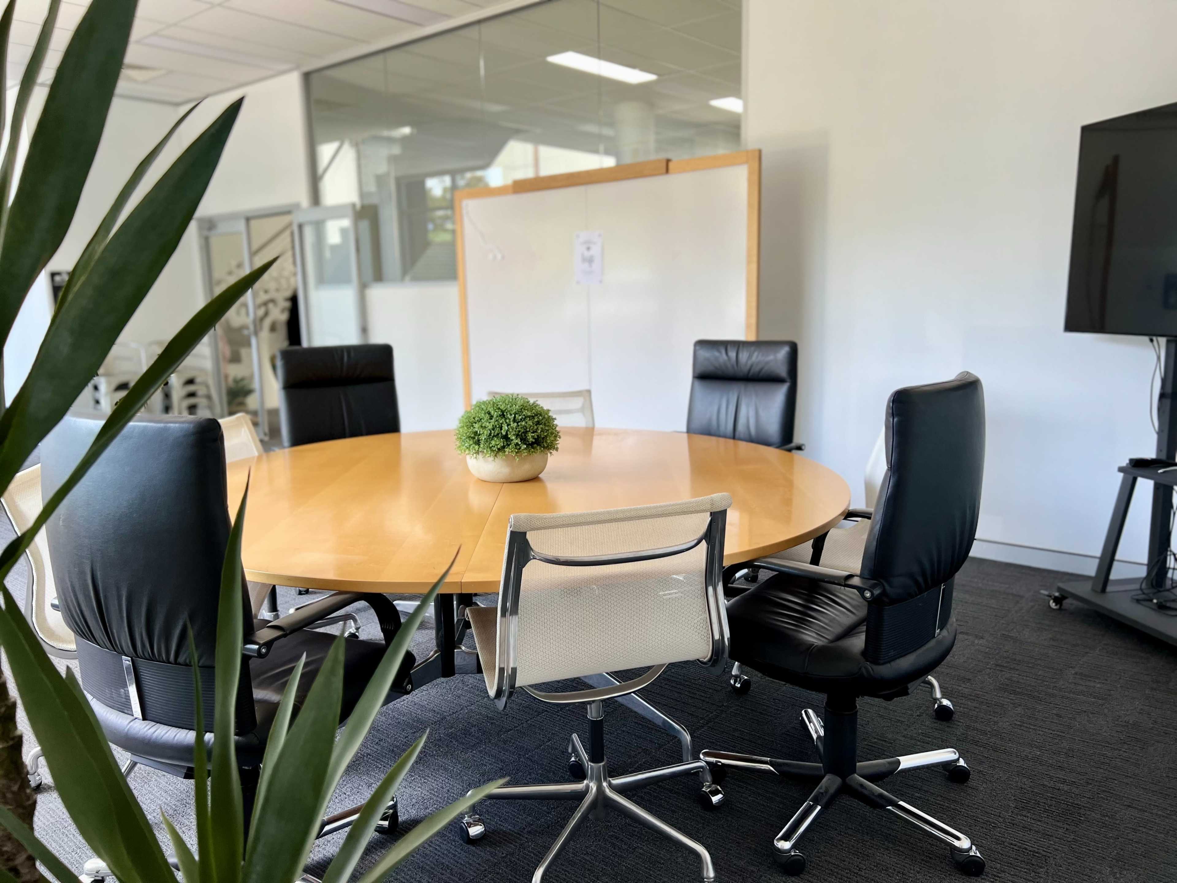 A round wooden conference table surrounded by six chairs in a modern meeting room.