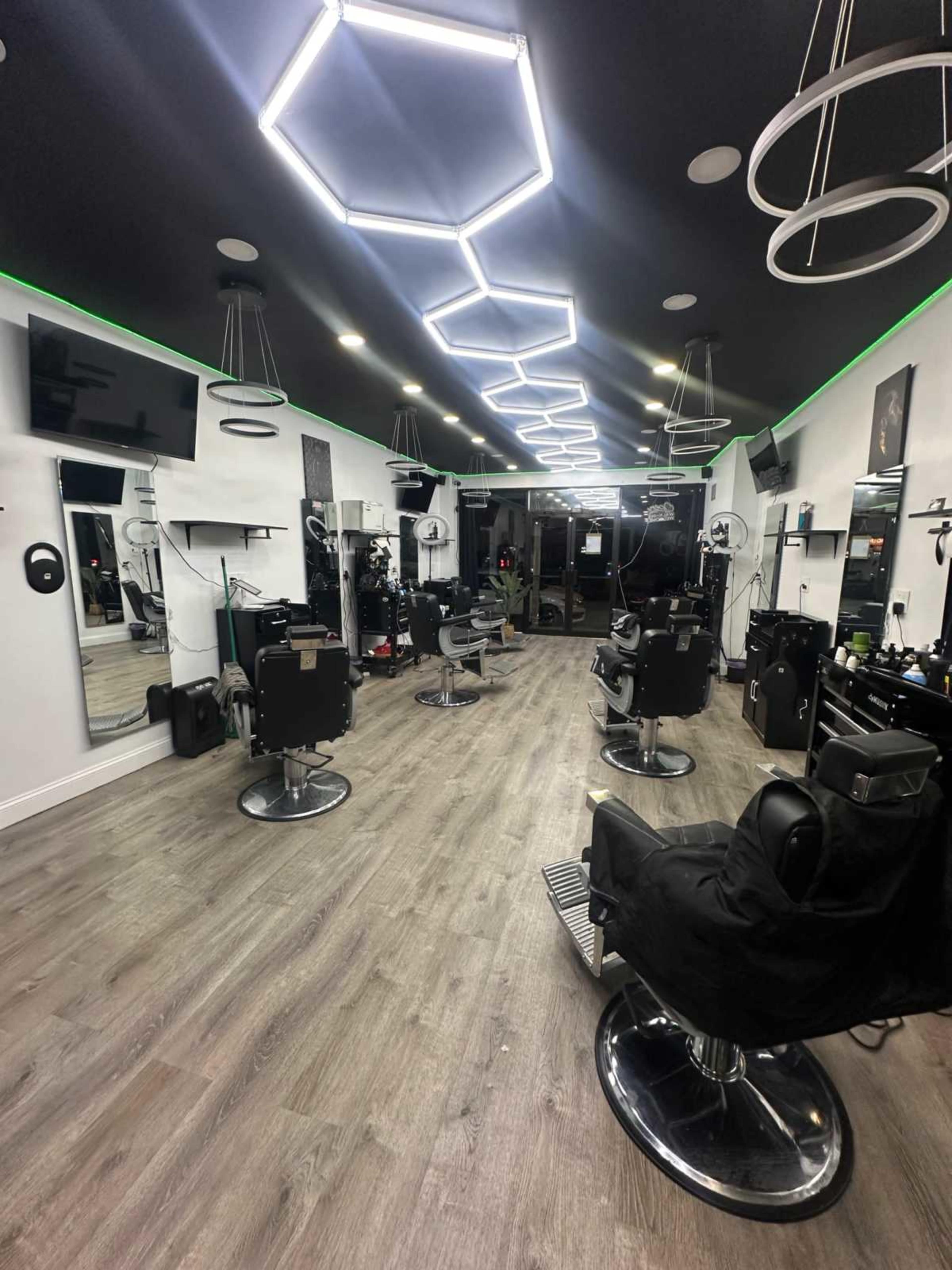 The image depicts a modern barbershop with multiple styling chairs, large mirrors, and overhead lighting in a geometric design.
