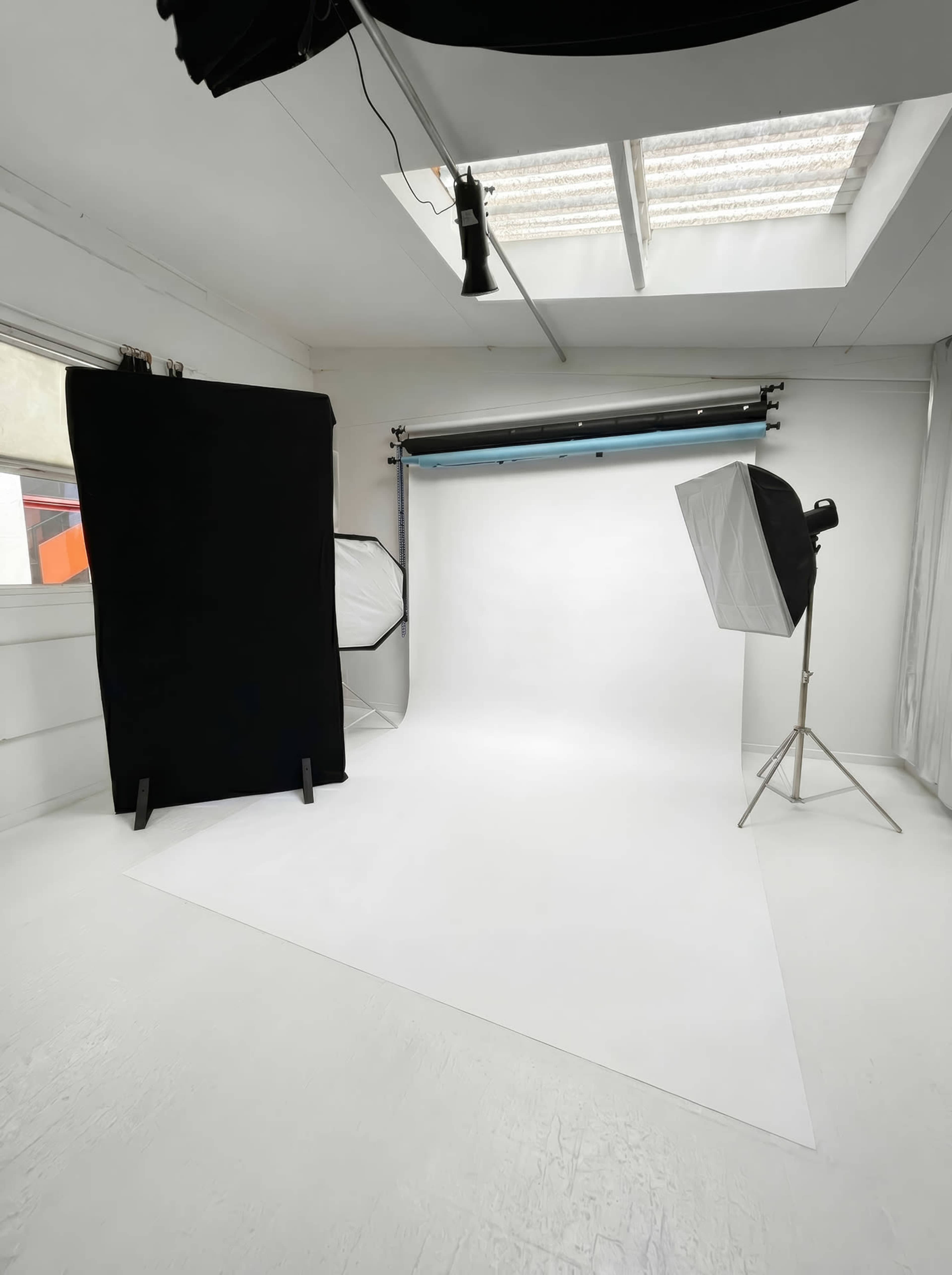 The image shows a photography studio featuring a white backdrop, various lighting setups, and a black curtain on the side.