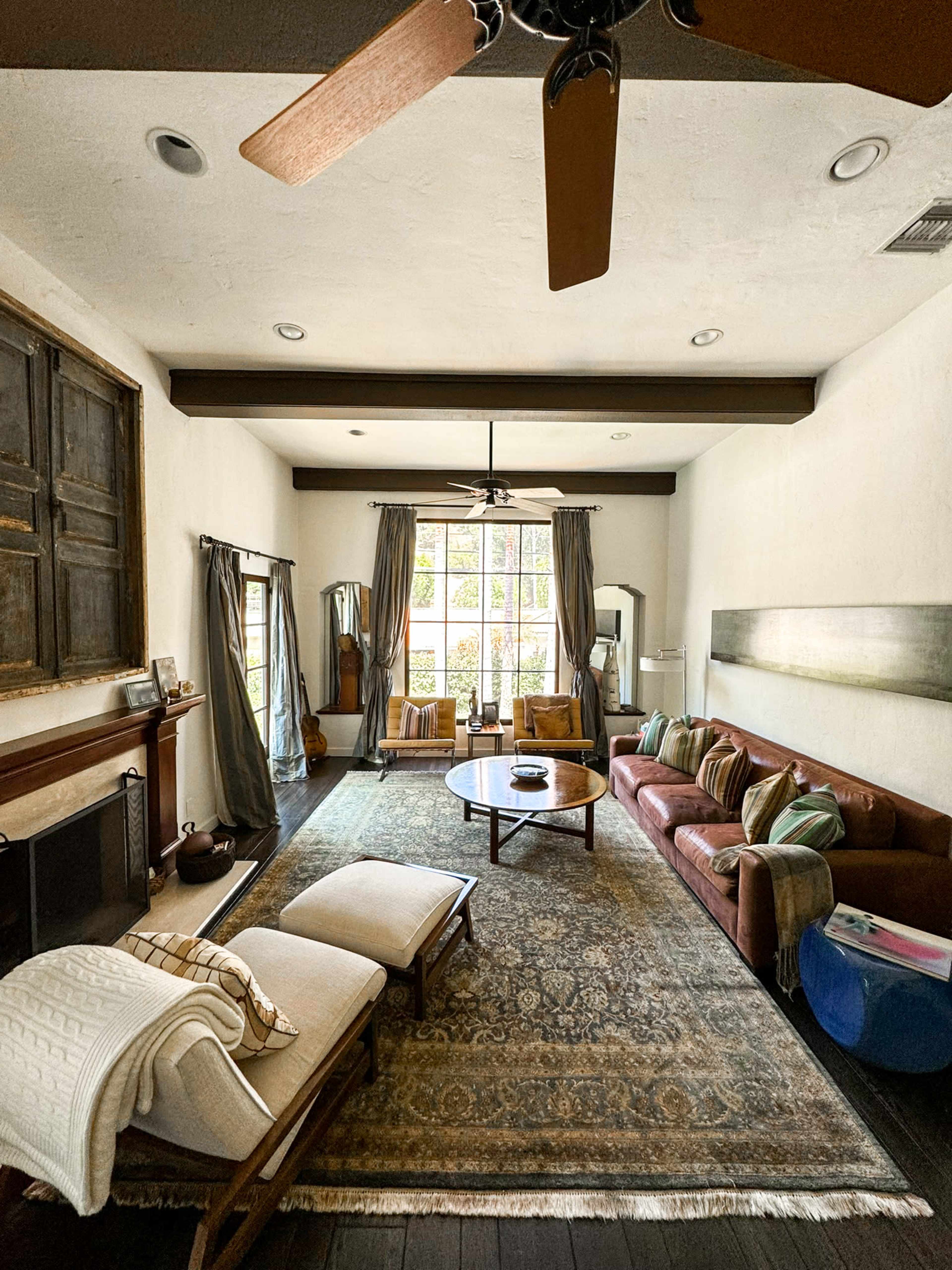 The living room features a large window, a brown couch, a wooden coffee table, and two lounge chairs, with a ceiling fan overhead.