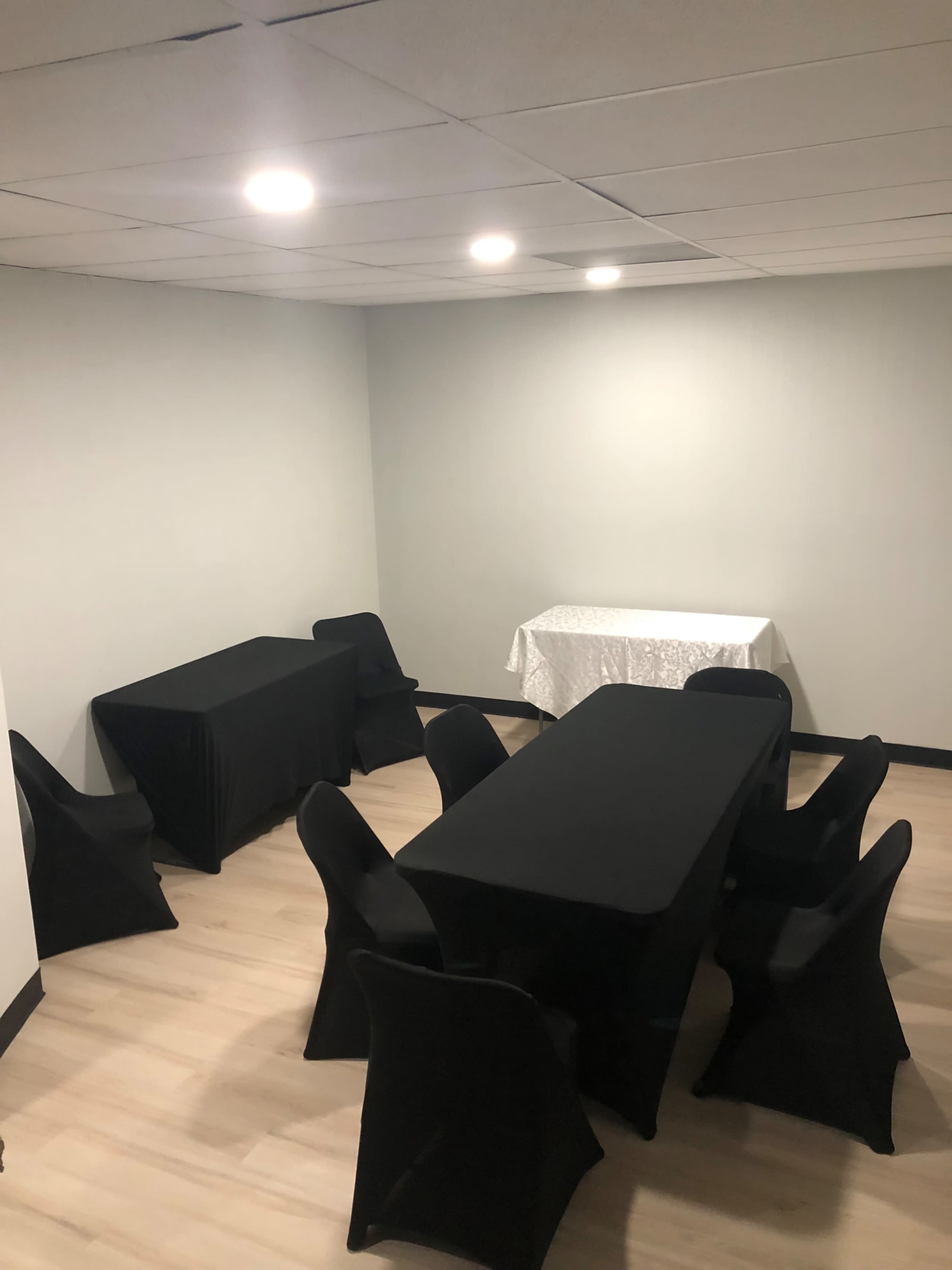 The image shows a room with three tables covered in black and white tablecloths, surrounded by black chairs, and illuminated by overhead lights.