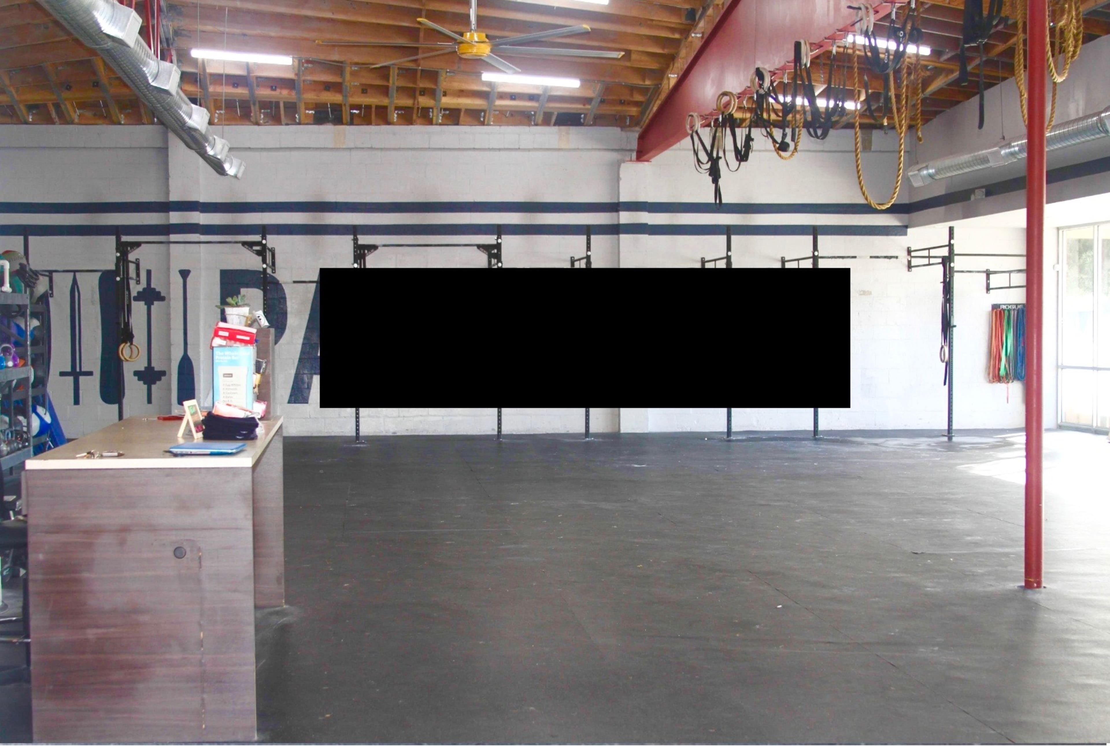 An empty gym space with wall-mounted equipment racks and a reception desk in the foreground.