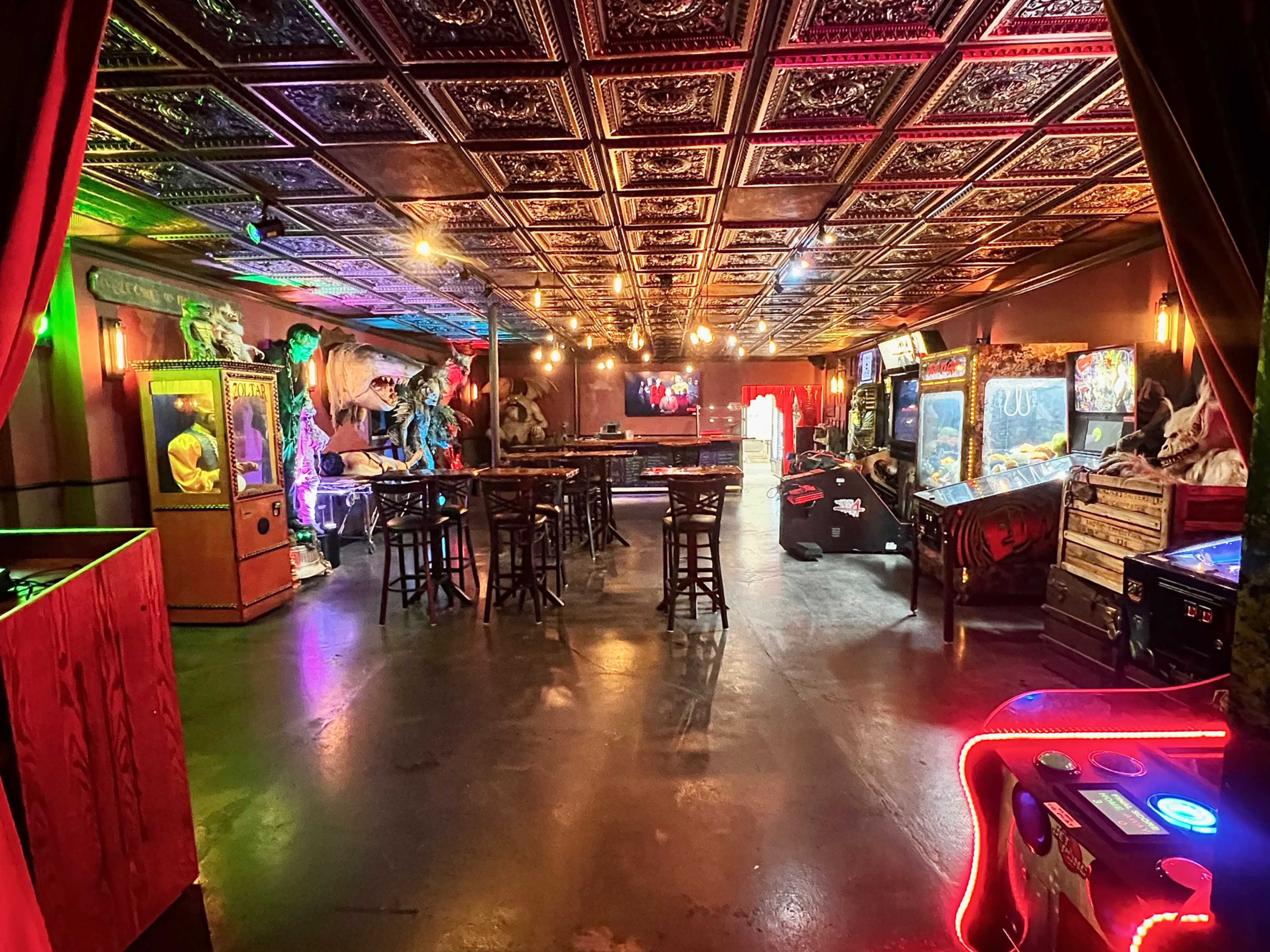 The image shows a spacious arcade room with vintage games, a bar area, and decorative lighting on the ceiling.