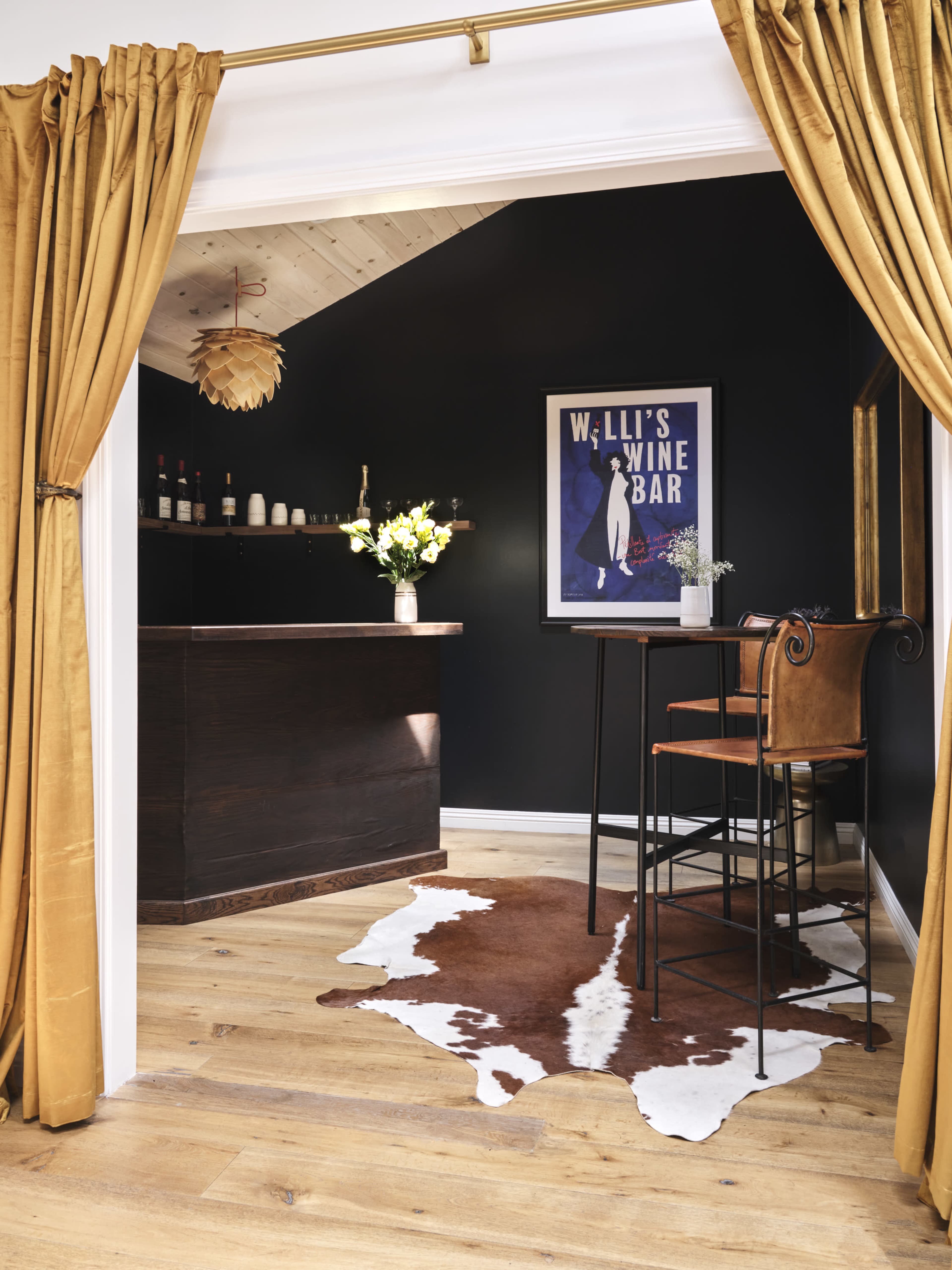 A small wine bar area features a dark wall, a wooden counter with bar stools, and a patterned cowhide rug on the floor.