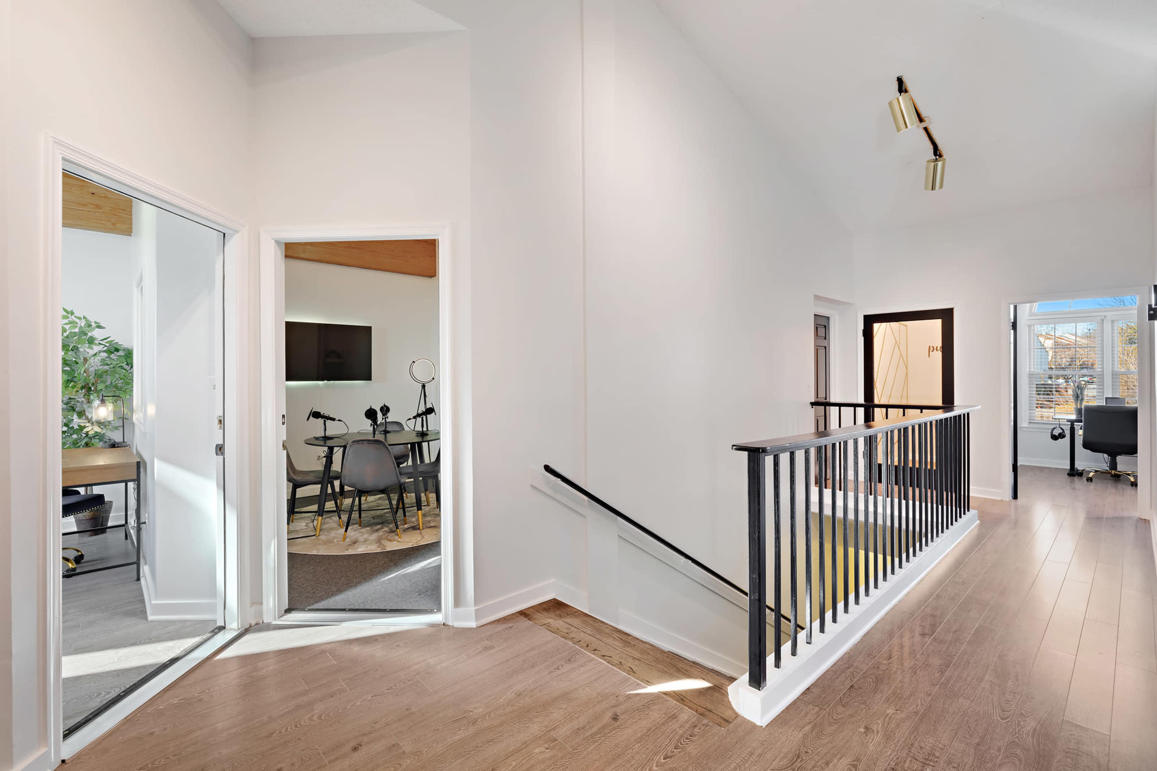 The image shows a well-lit hallway leading to a meeting room on the left and an office space on the right, with a staircase in the center.