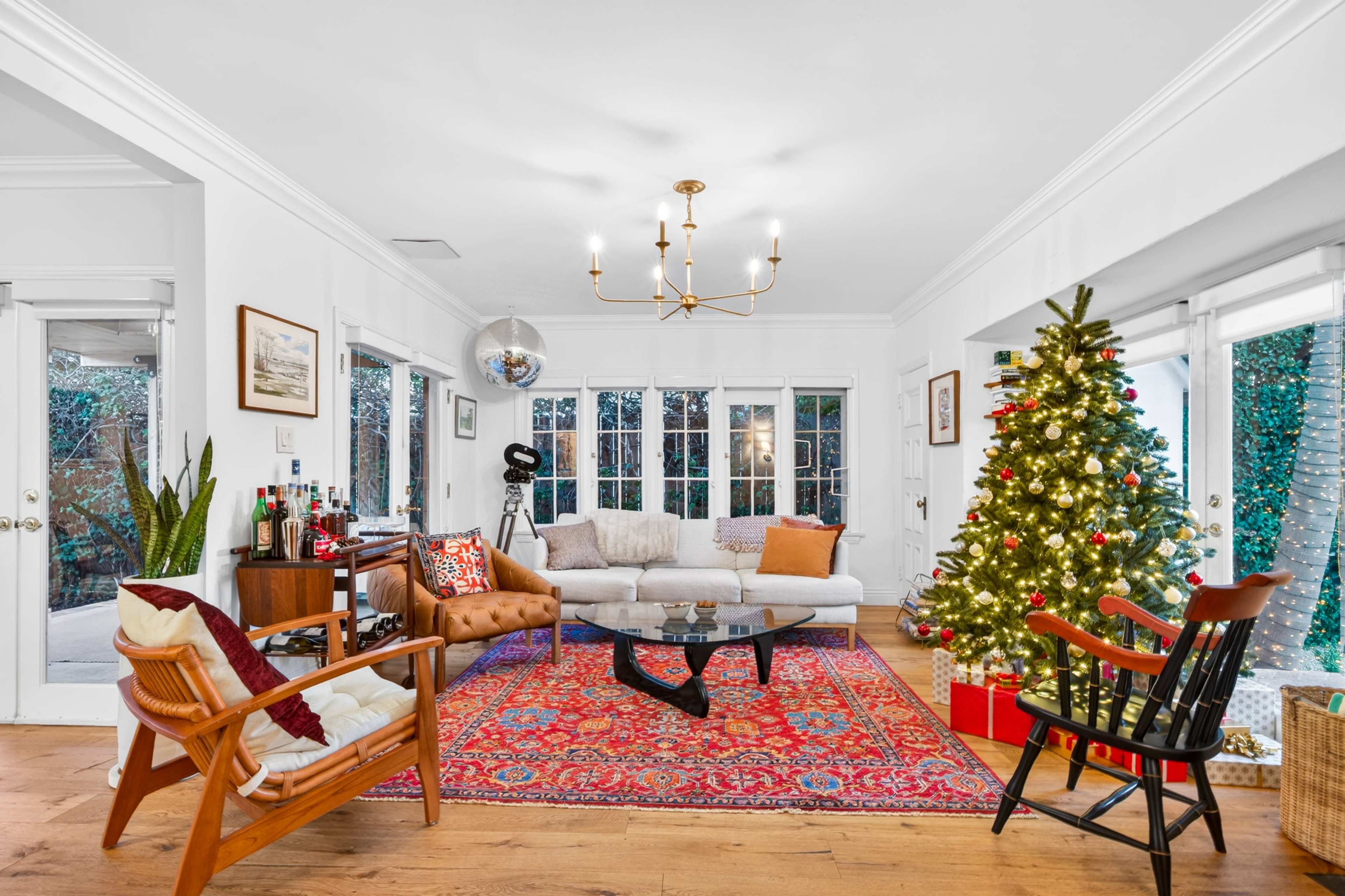 A cozy living room features a decorated Christmas tree, a modern chandelier, and large windows with natural light.