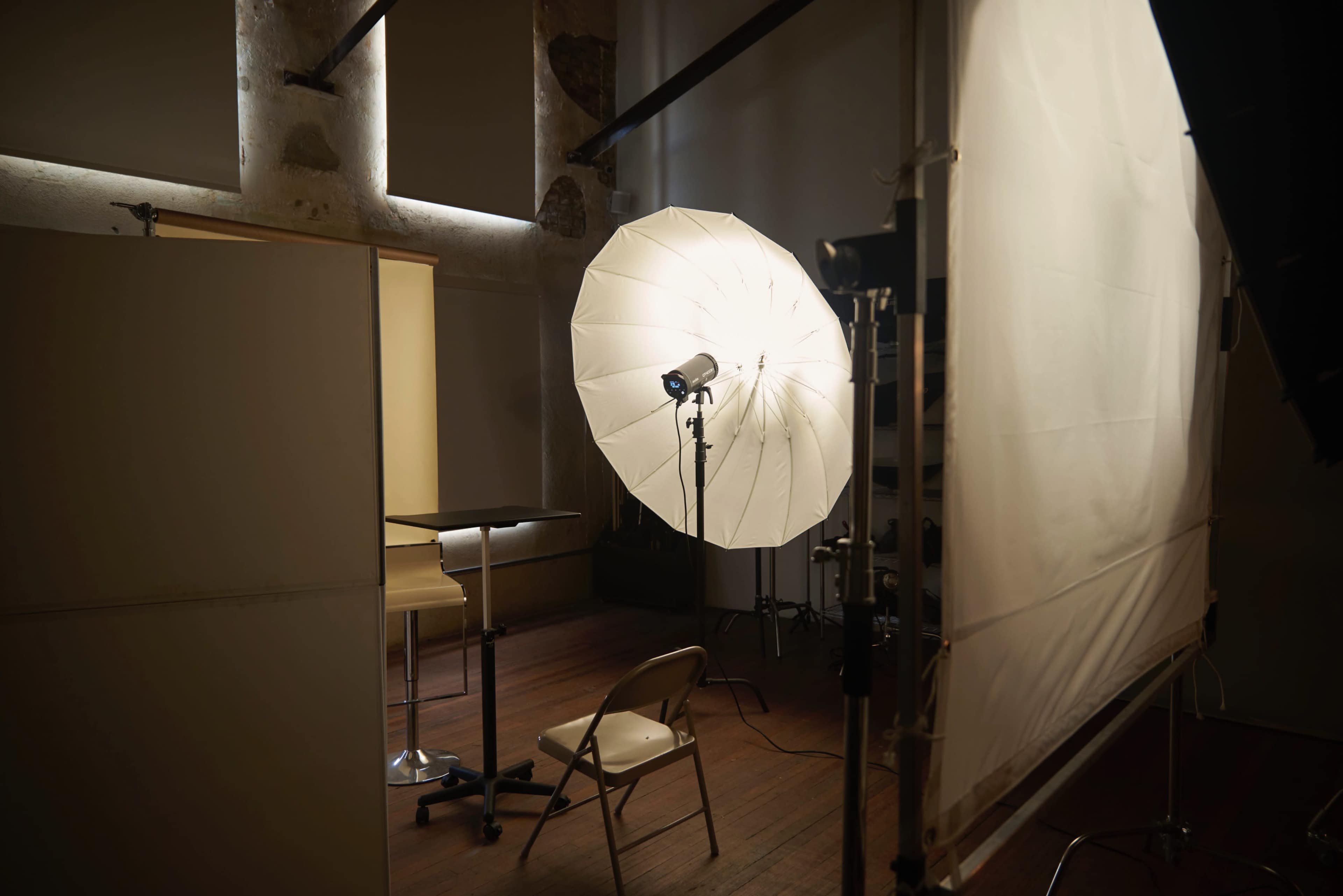 A photography studio is set up with a large softbox light, a chair, and a table against a textured wall.