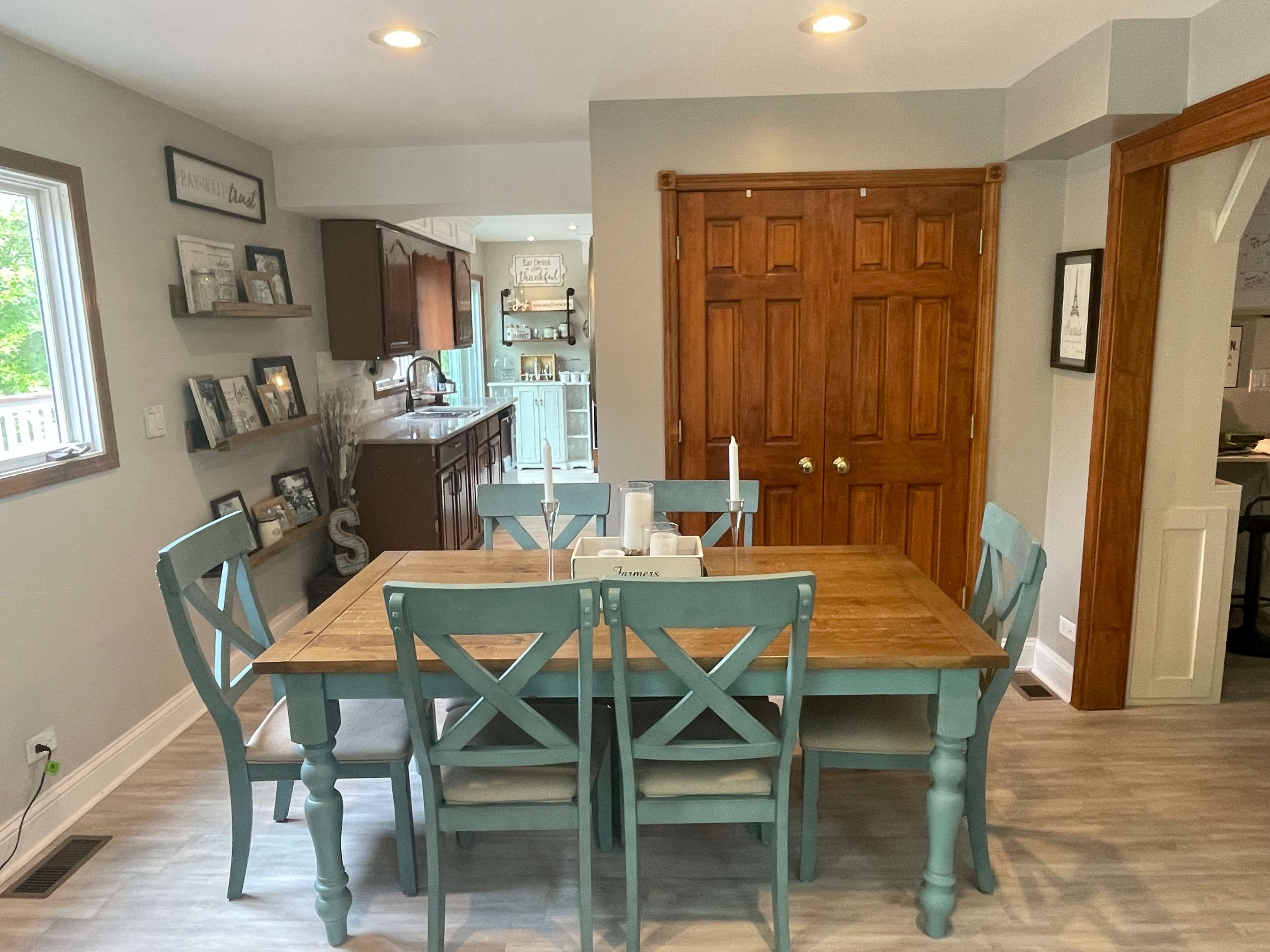 A spacious dining area features a wooden table surrounded by blue chairs, with a doorway leading to a kitchen visible in the background.