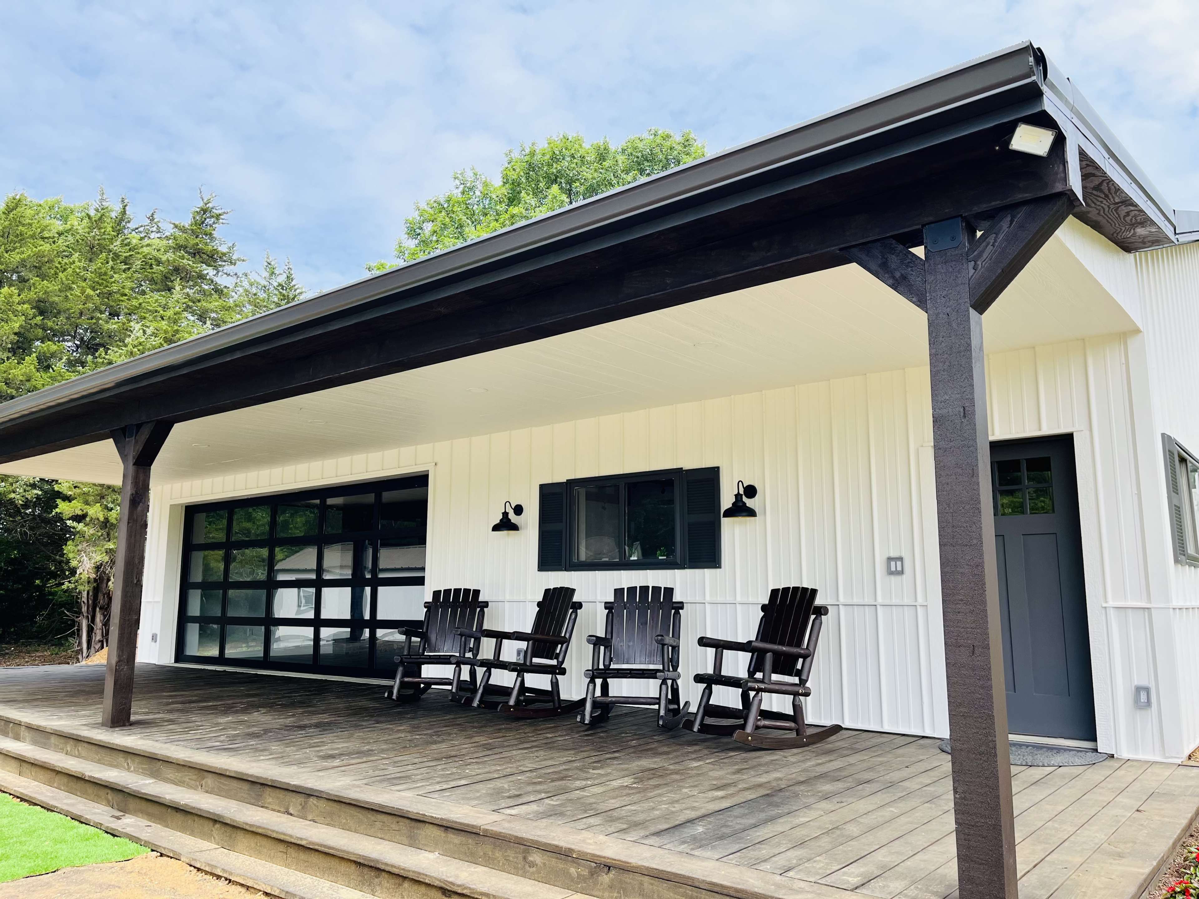 A modern home features a covered porch with wooden rocking chairs and a large glass garage door.