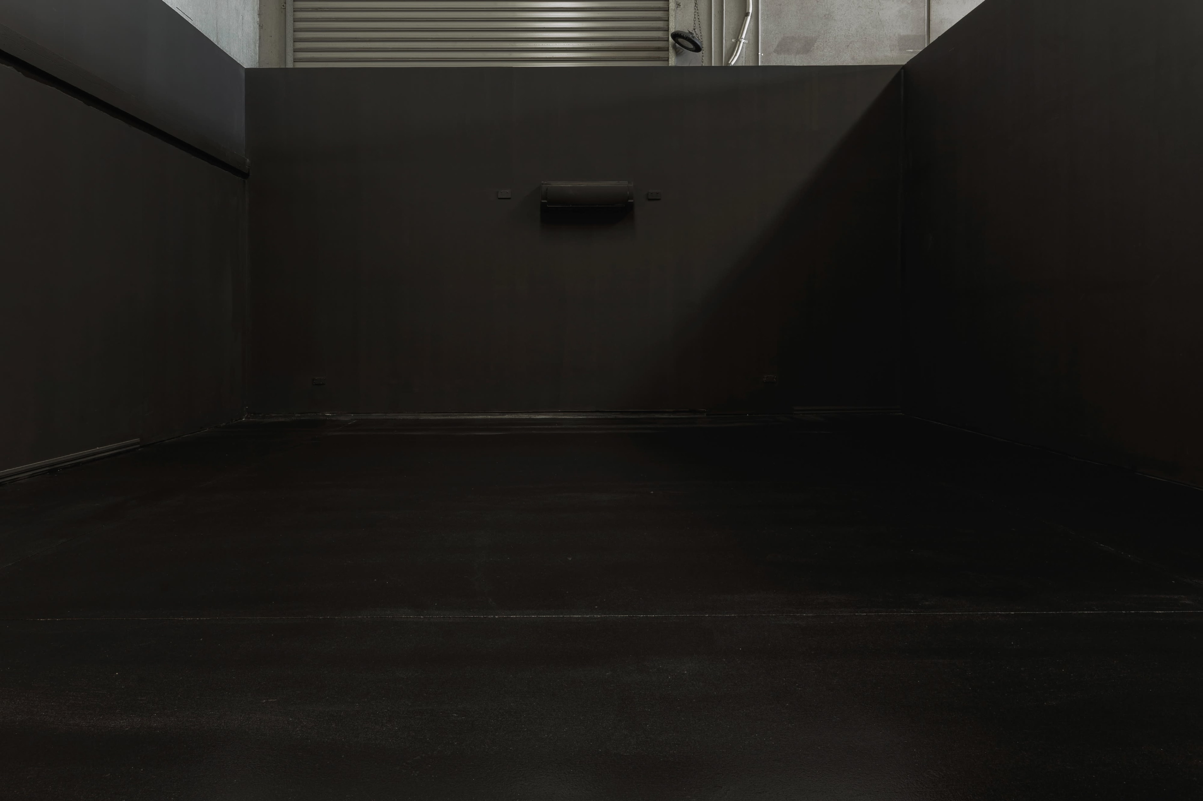 The image shows an empty, dimly lit room with dark walls and a smooth black floor.
