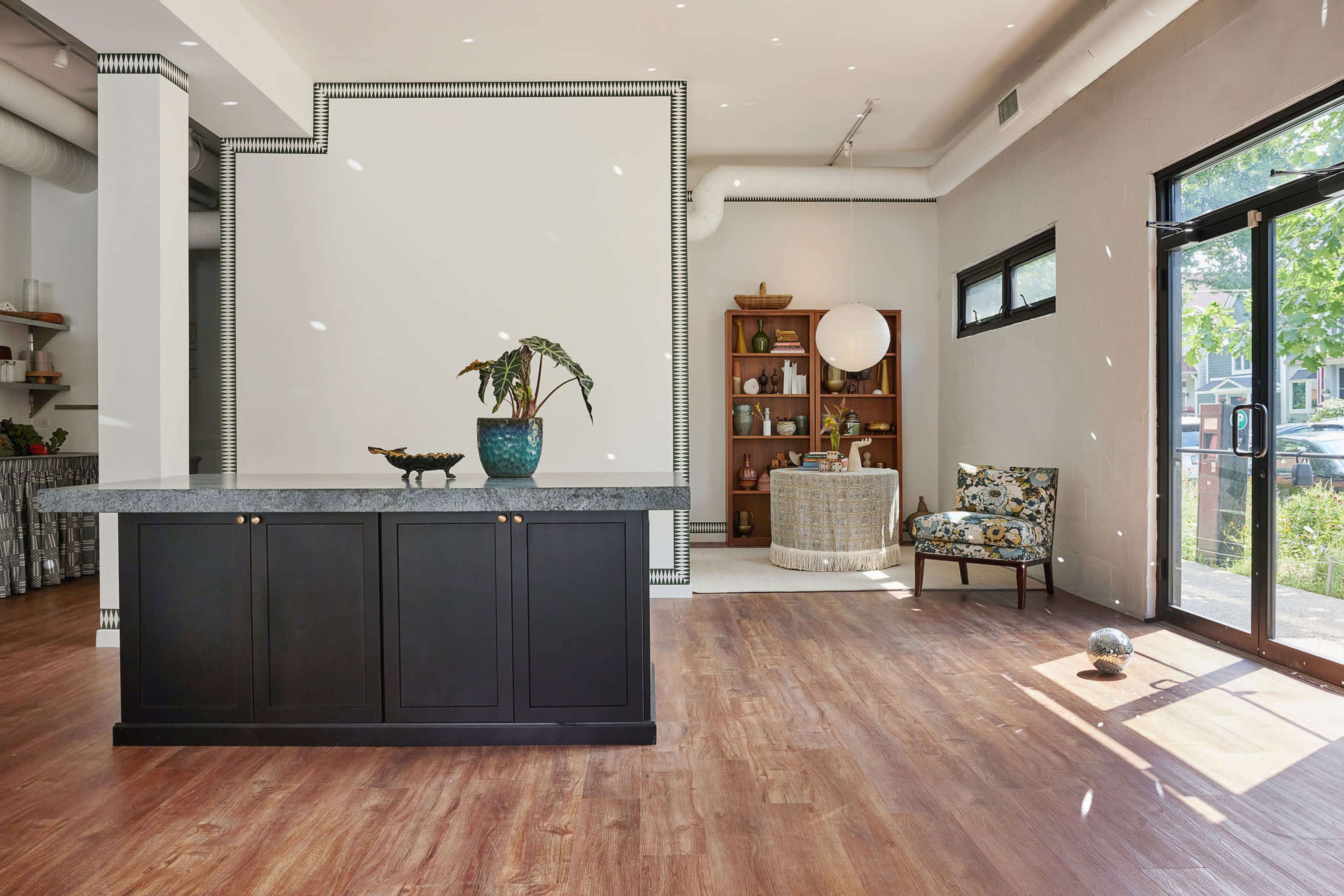 A spacious interior with a black reception counter, a decorative plant, and a stylish seating area featuring floral upholstery.