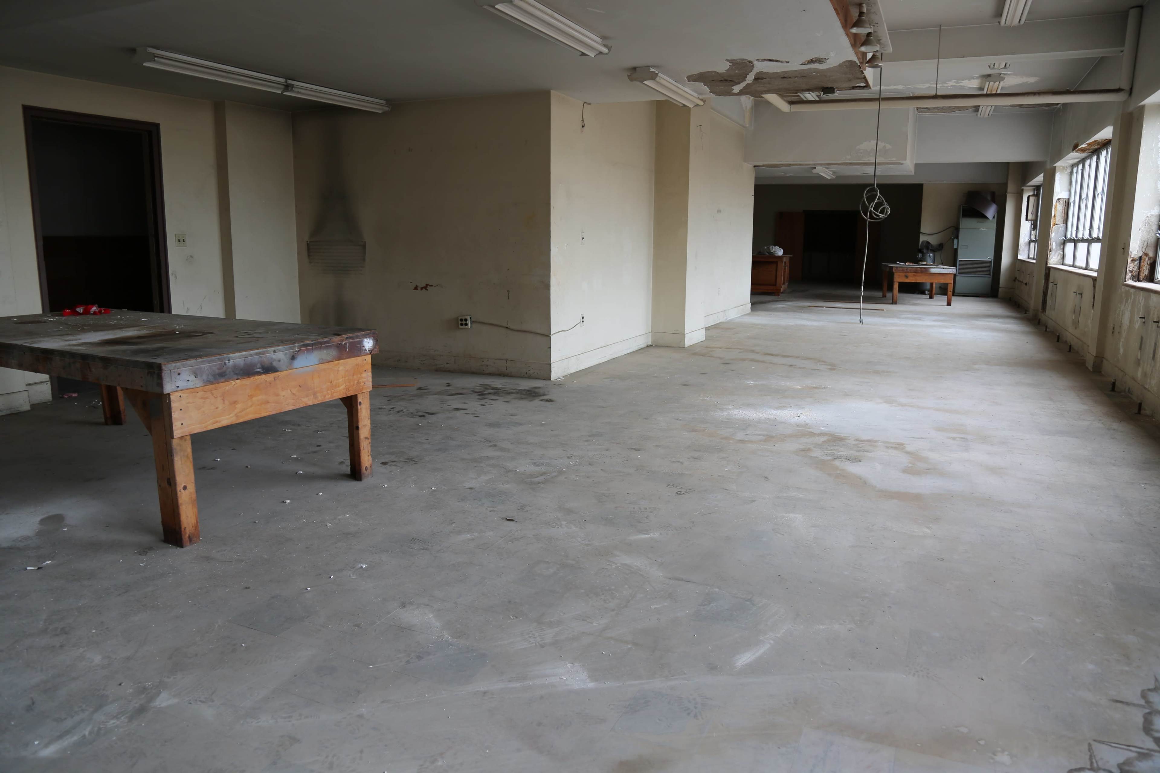 An empty room features bare concrete floors, walls in need of repair, and a few scattered pieces of furniture.