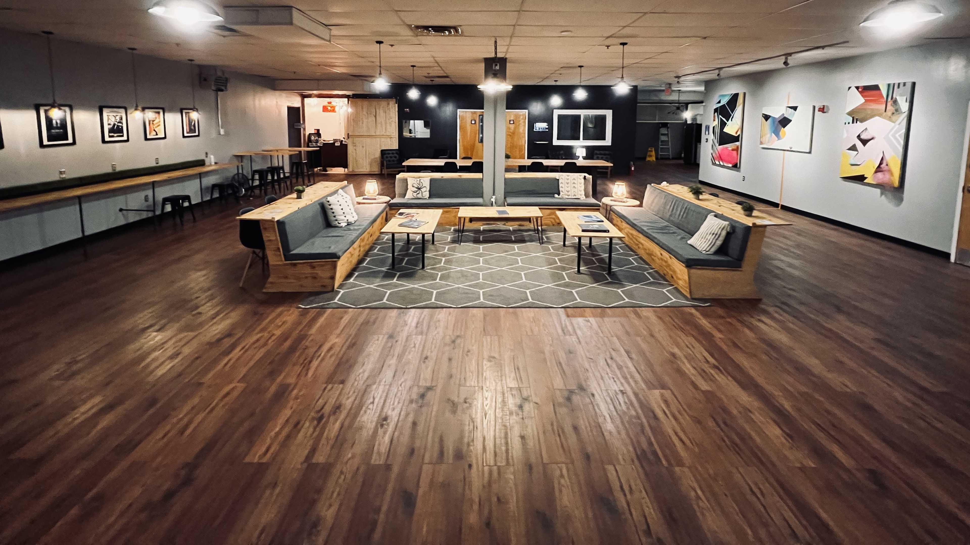 A spacious, modern lounge area featuring sectional seating, wooden tables, and artwork on the walls, along with a patterned rug on a hardwood floor.