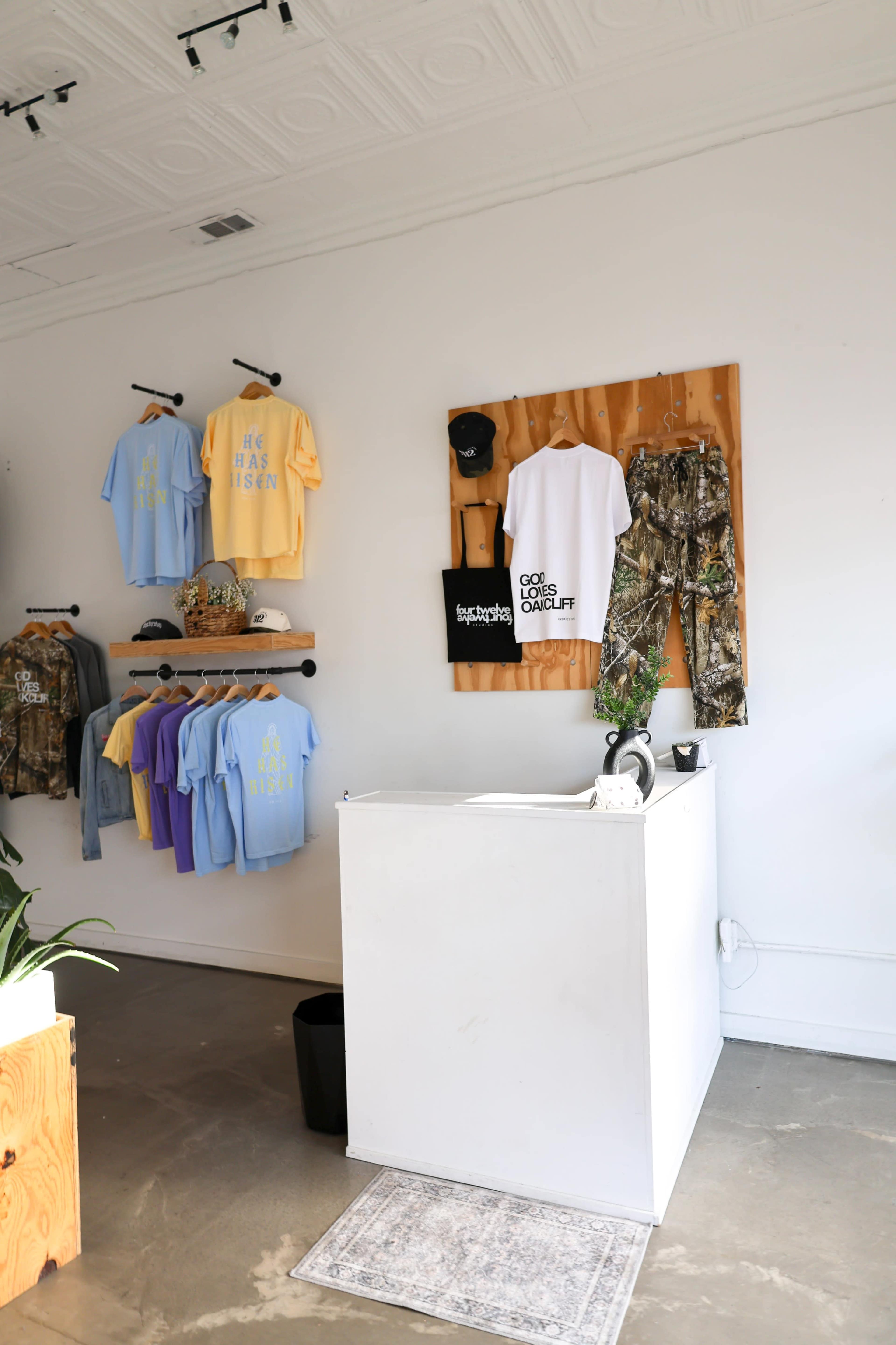 A retail space displays hanging apparel in pastel colors and camouflage, with a white sales counter and decorative wall decor.