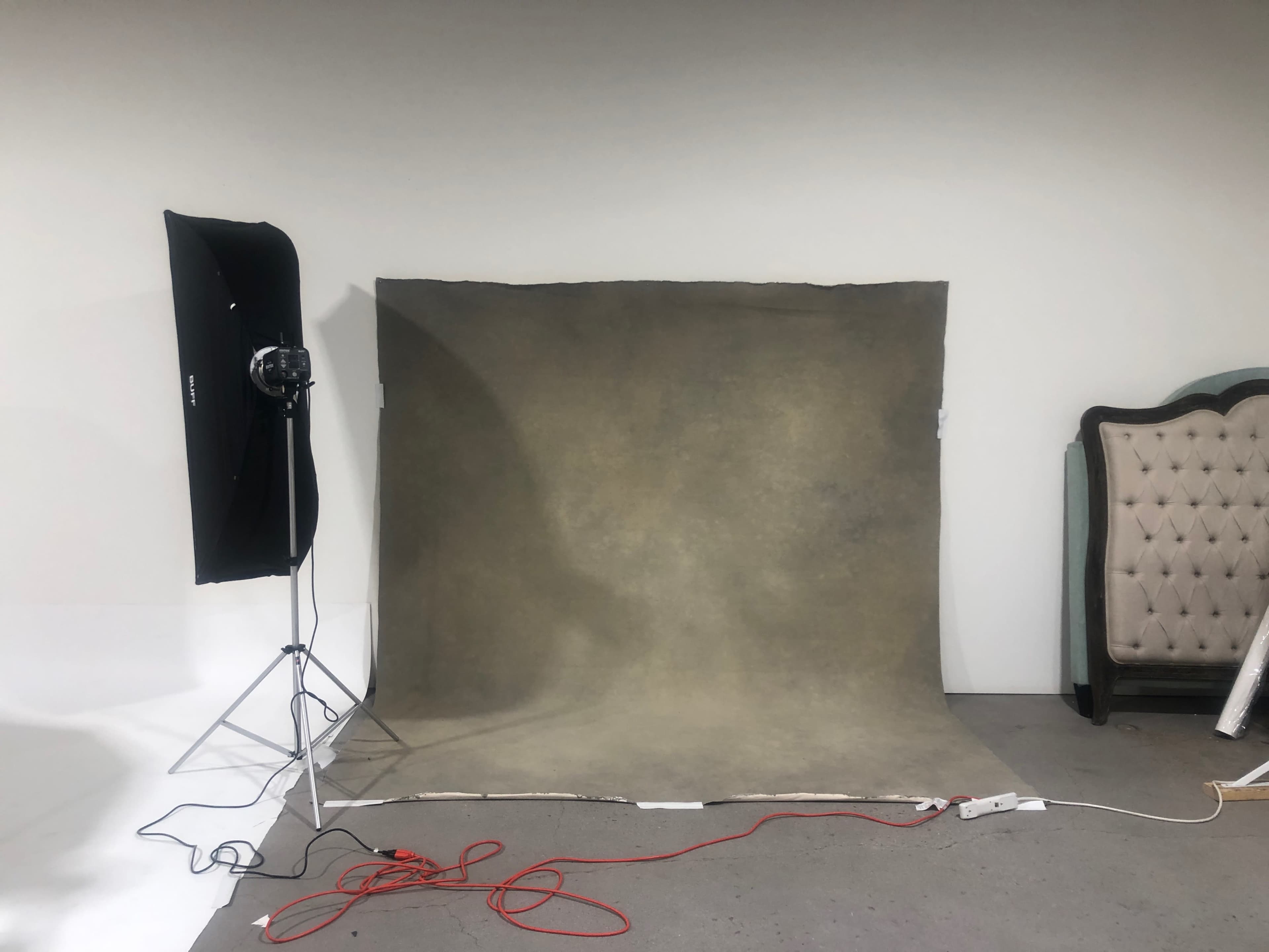 A photography setup featuring a gray backdrop with studio lighting on one side and a vintage-style chair in the corner.