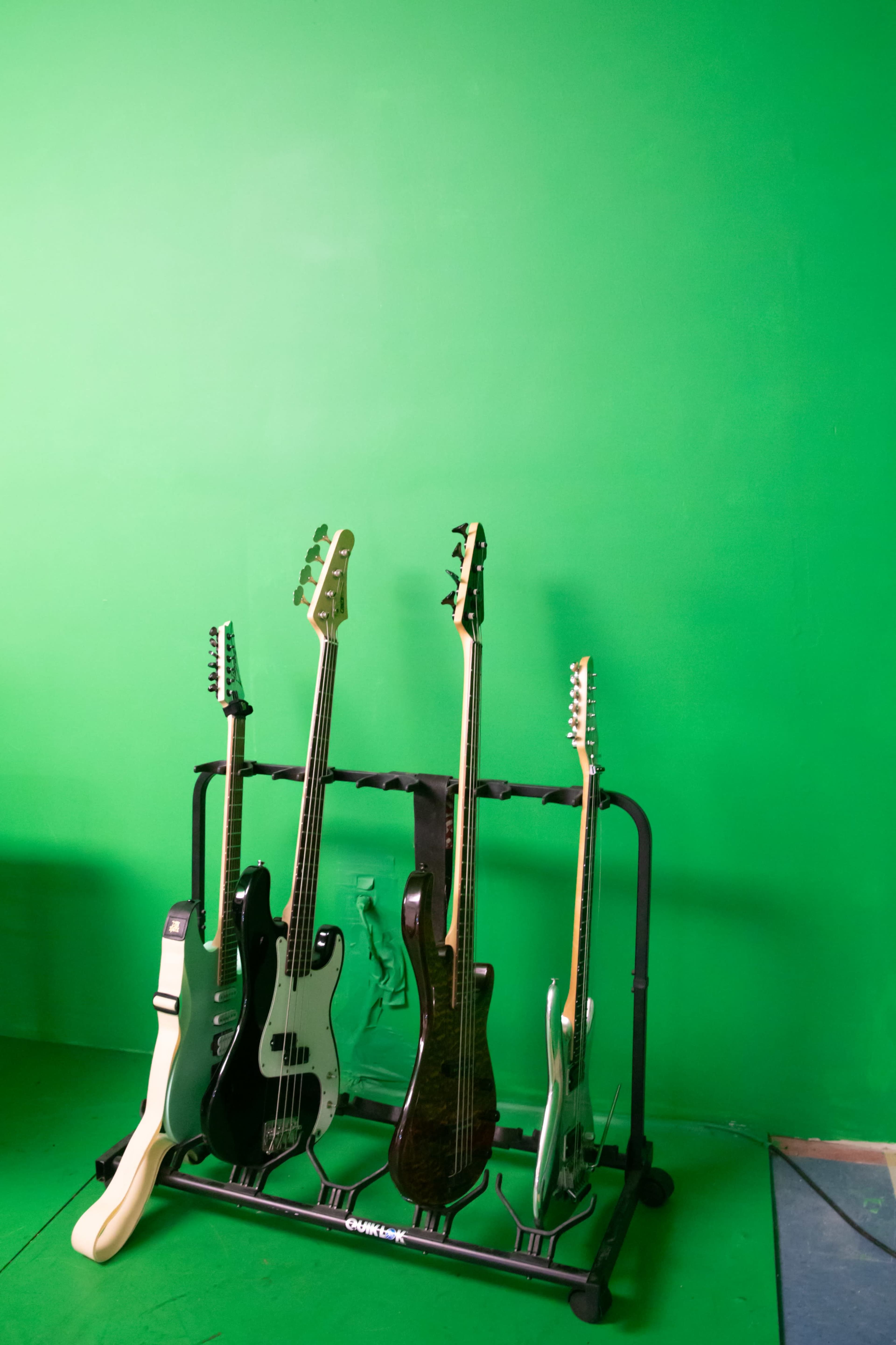 A rack holds several guitars against a bright green wall.