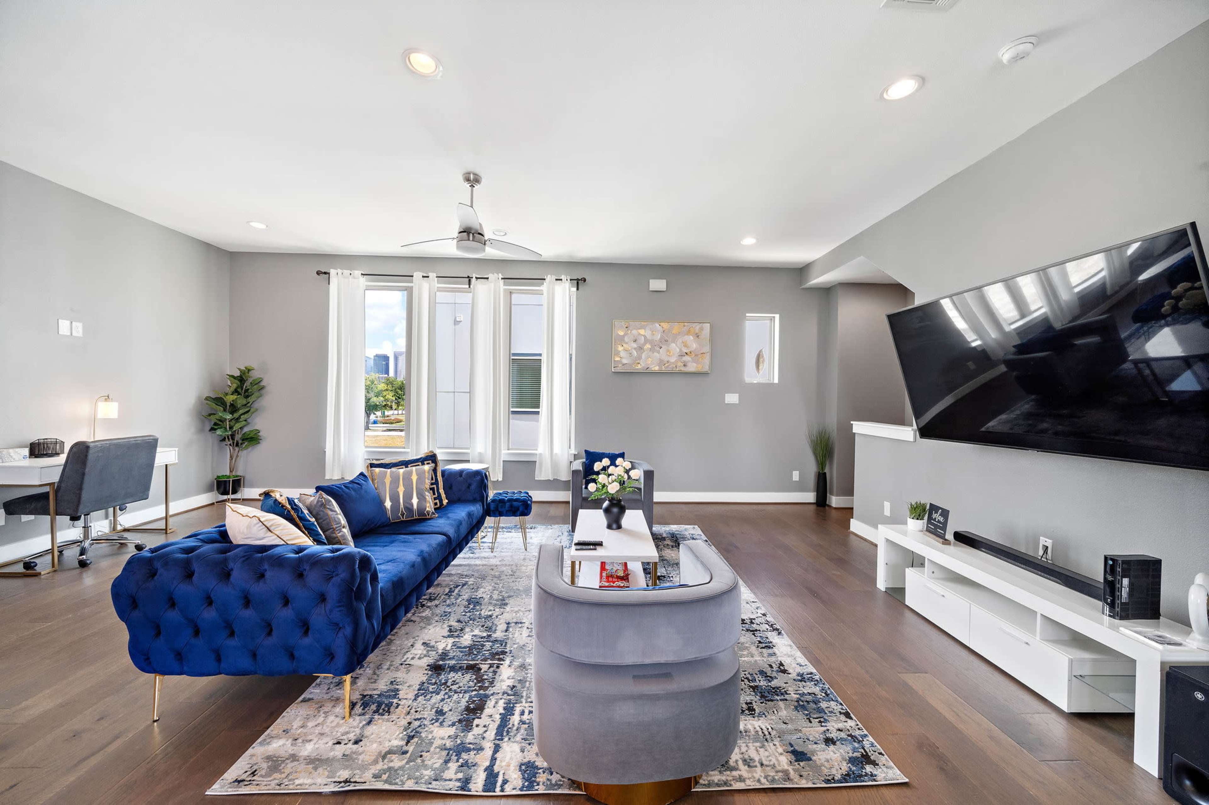 A modern living room featuring a blue tufted sofa, a decorative rug, and a large television mounted on the wall.