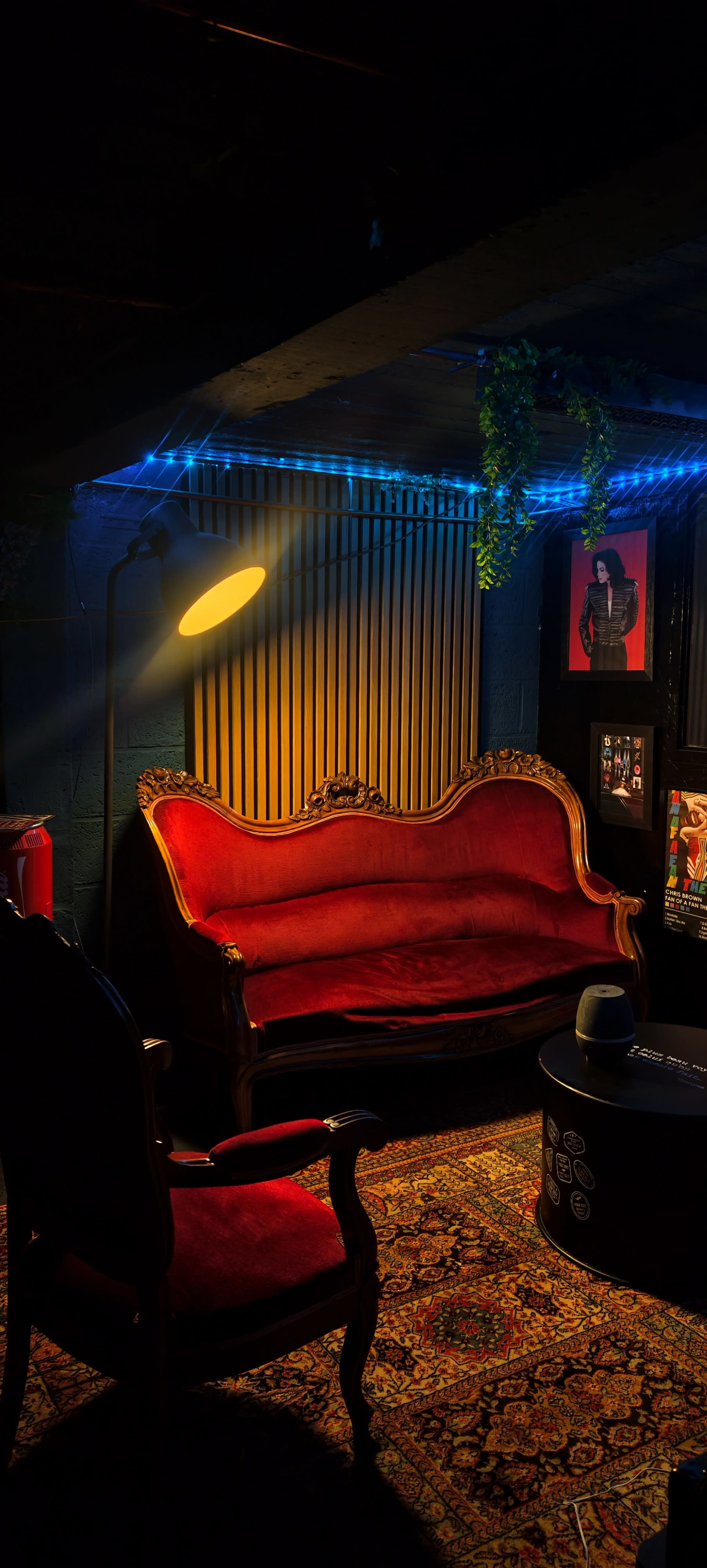The image shows a cozy room with a red vintage sofa, a floor lamp, and framed artwork on the walls, illuminated by soft blue LED lights.