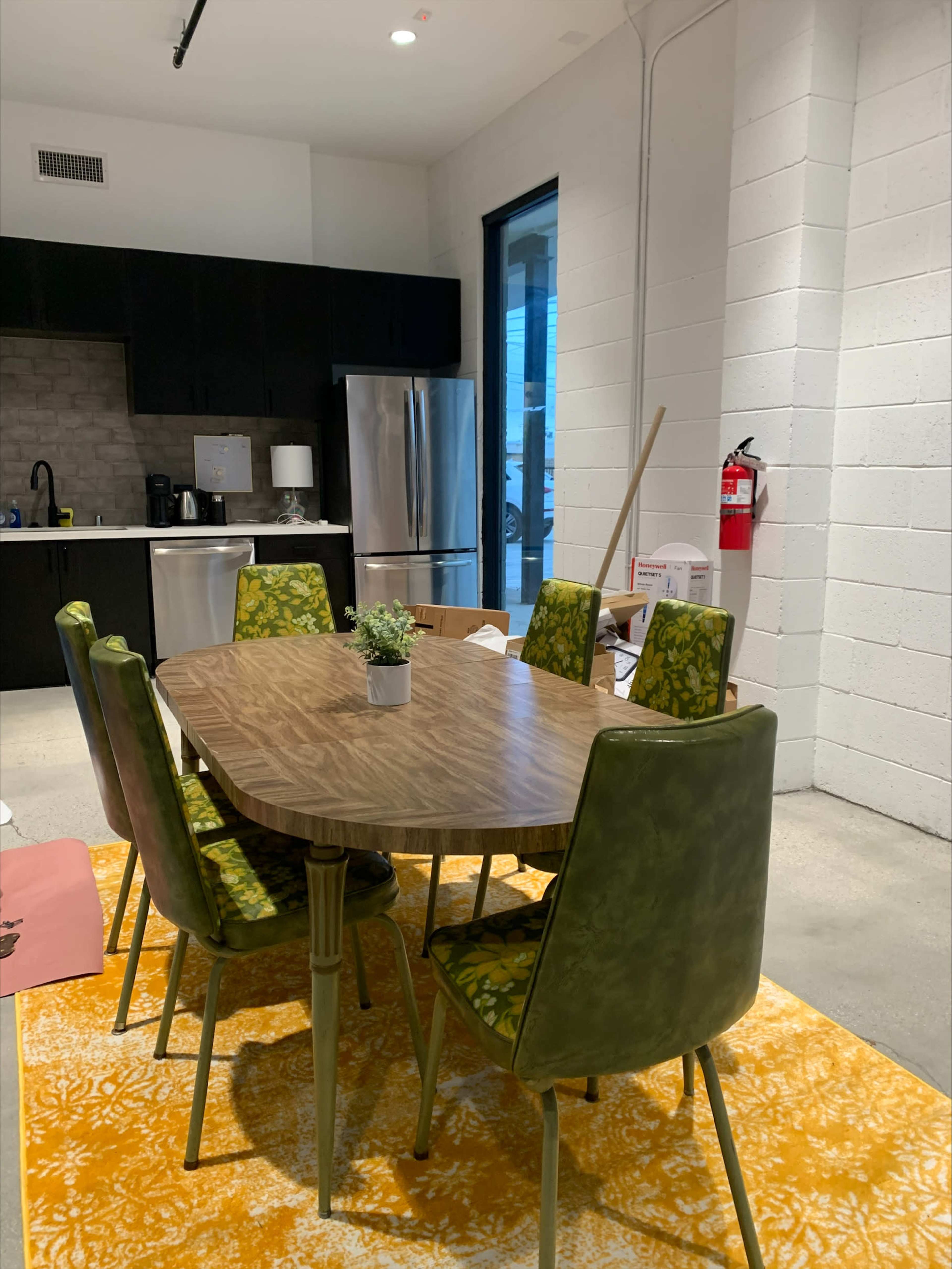 A wooden dining table surrounded by six green upholstered chairs is set in a modern kitchen area with gray walls and black cabinetry.