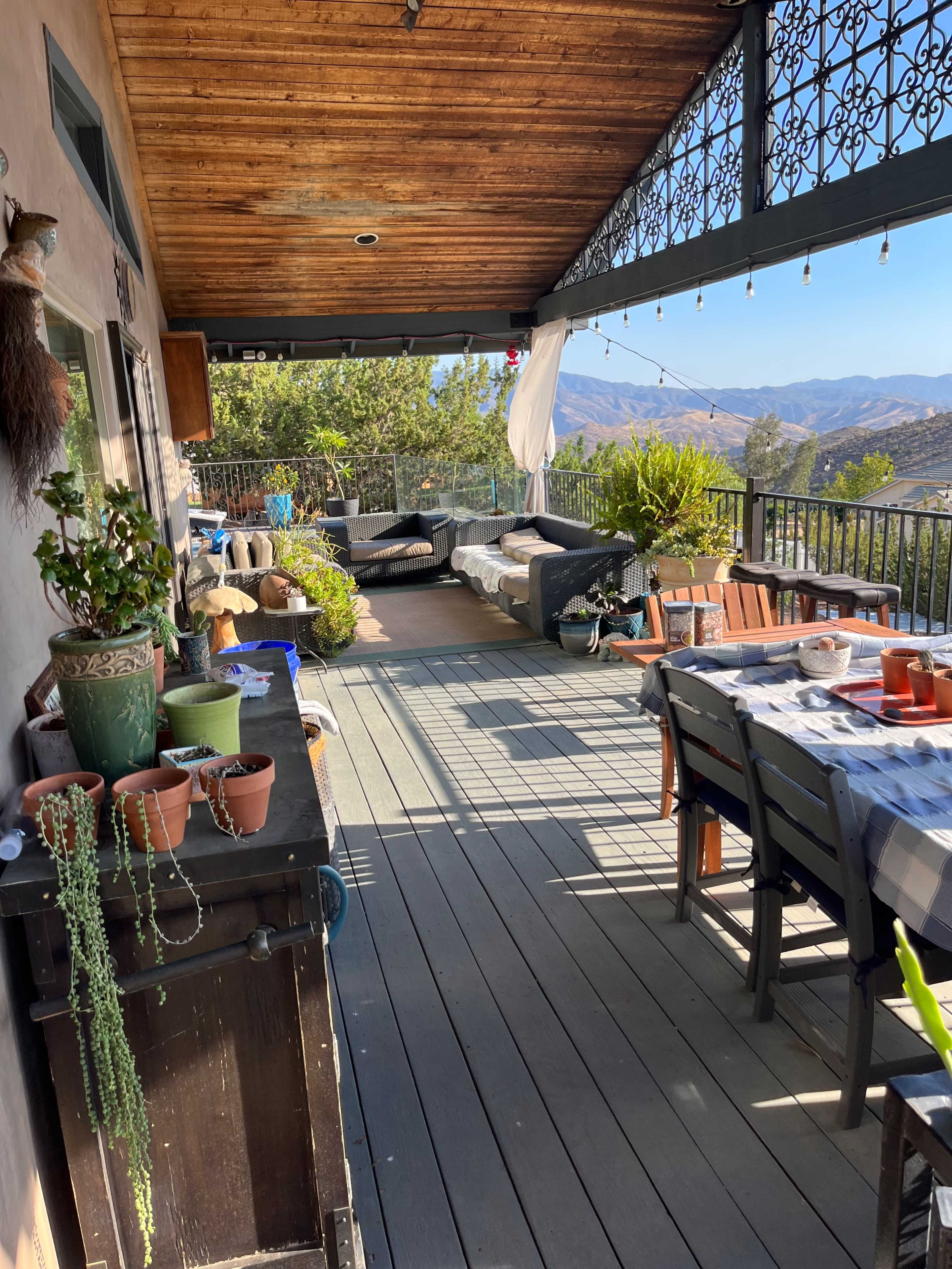 A outdoor patio features a dining table, potted plants, and seating areas with a view of distant mountains.