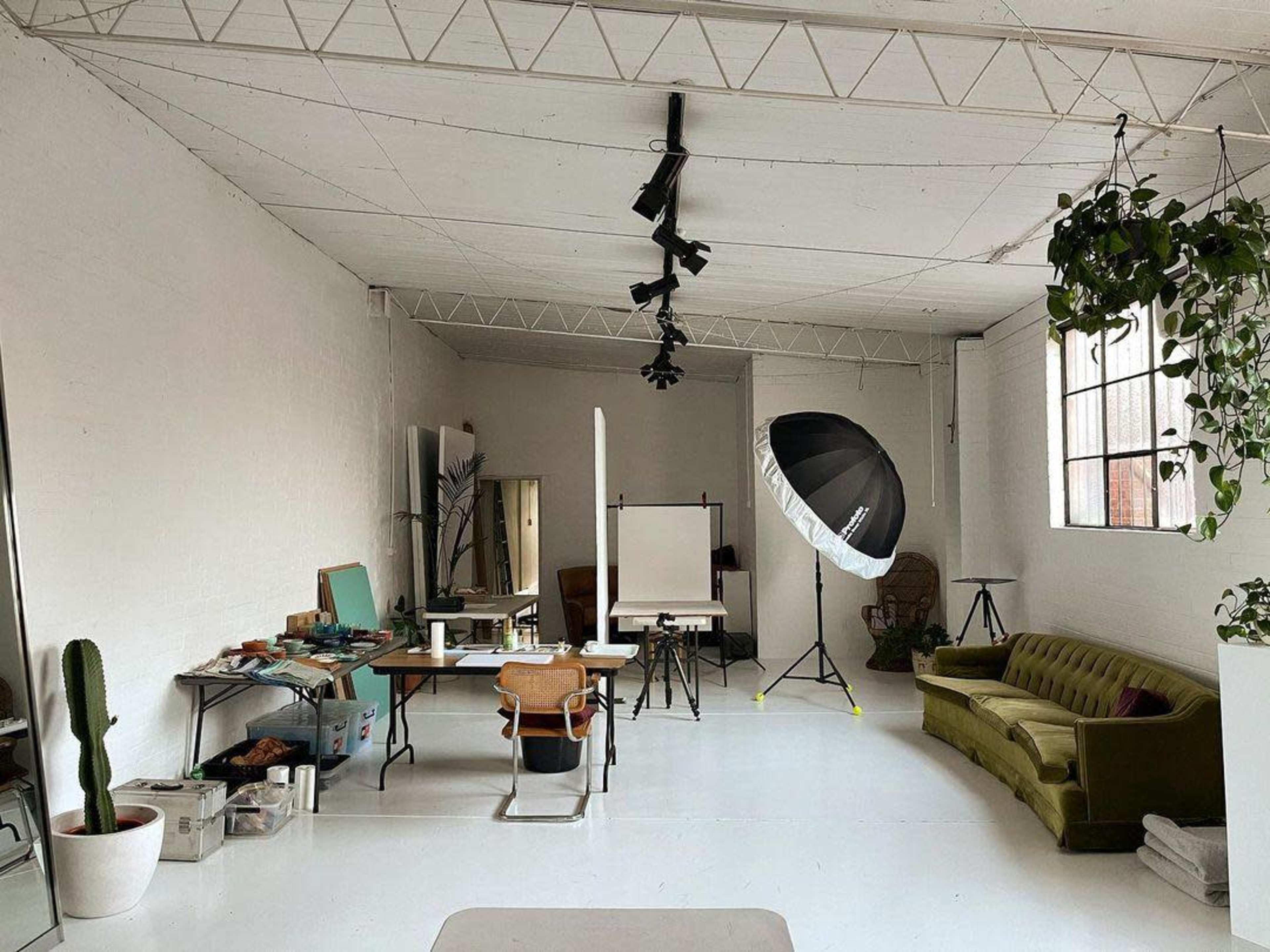 A spacious studio with a green sofa, a large photography light, and tables set up with various items for creative work.