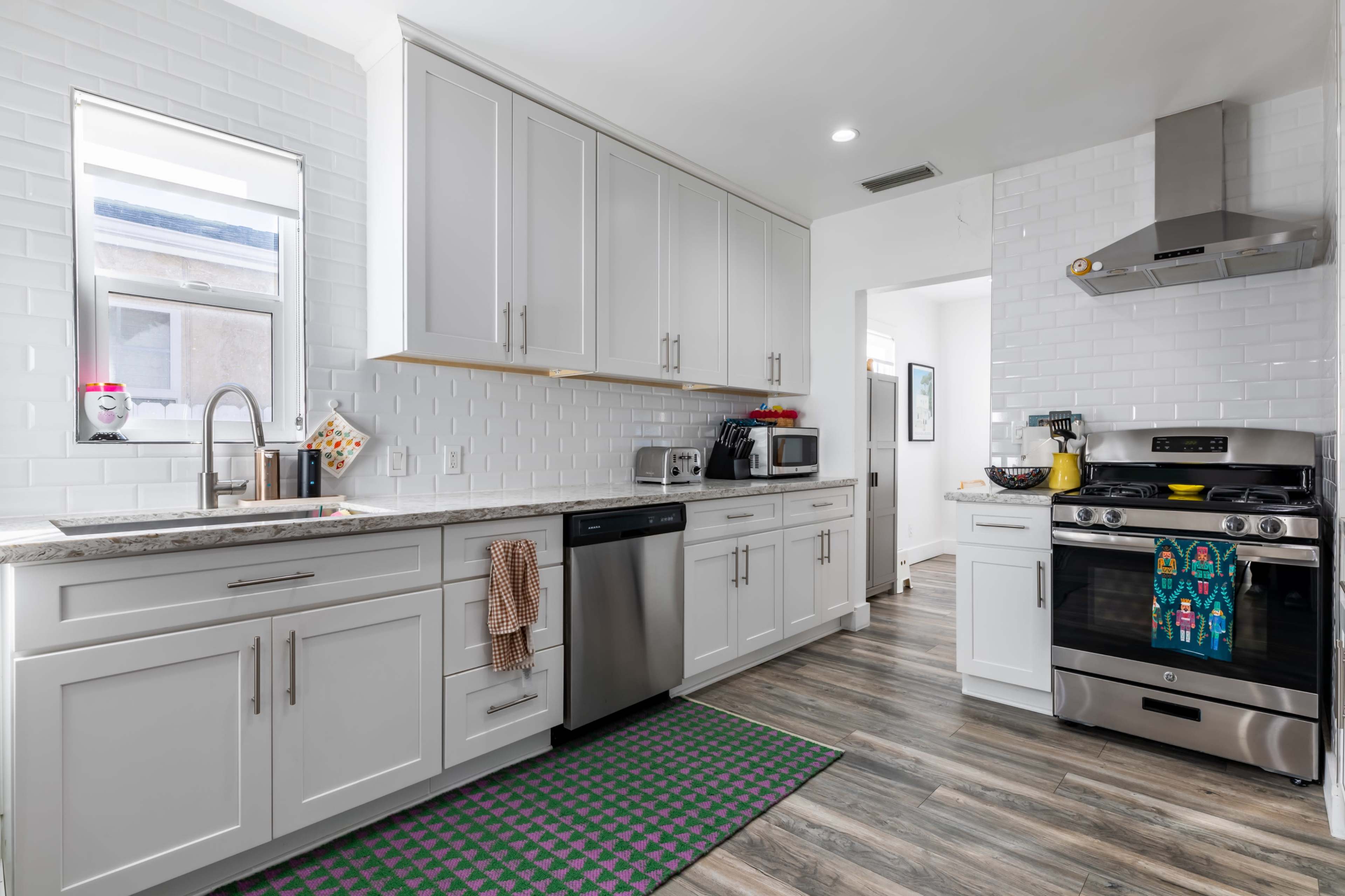 The image shows a modern kitchen with white cabinetry, stainless steel appliances, and a granite countertop.