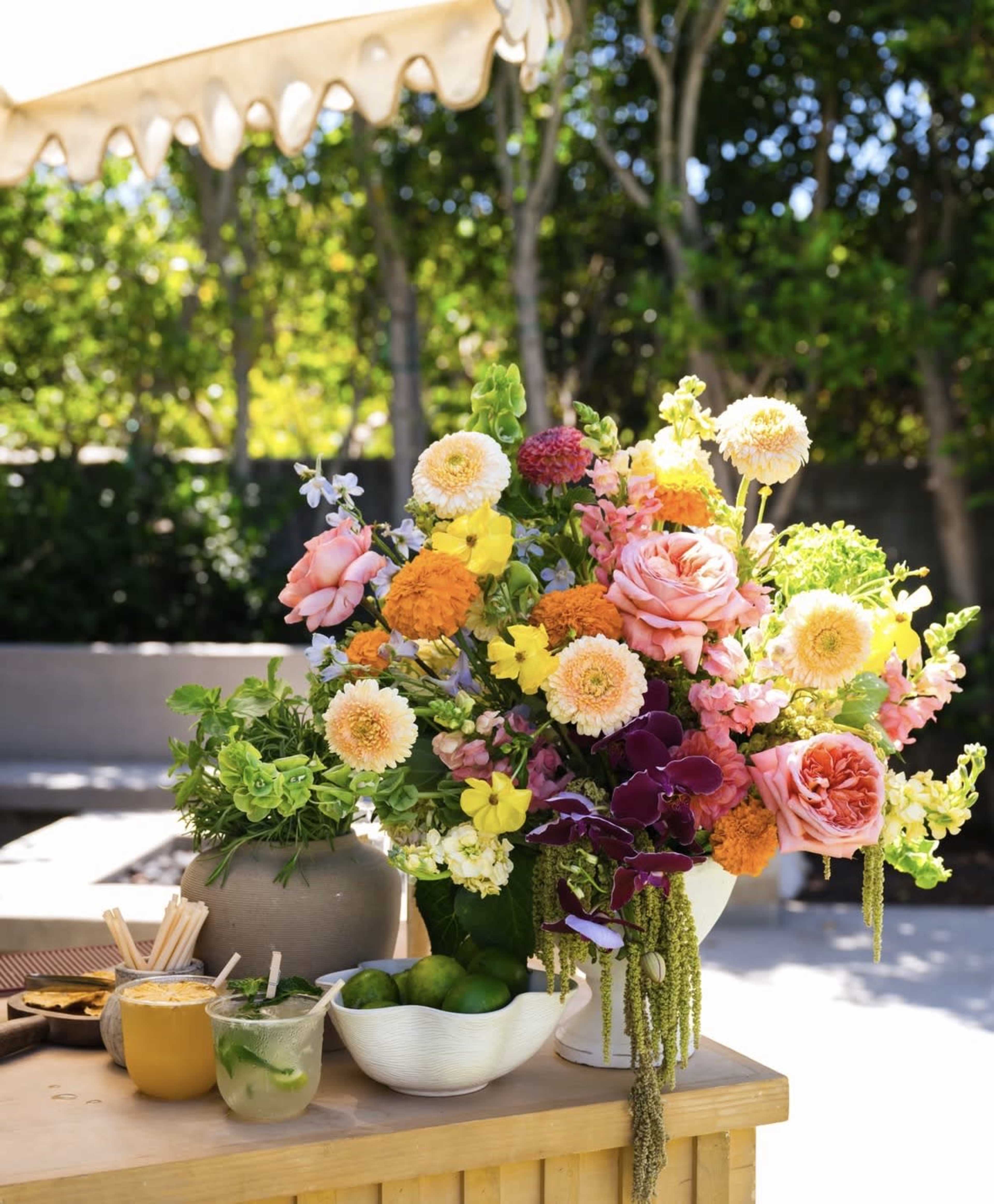 A vibrant arrangement of mixed flowers, including roses and marigolds, is displayed on a wooden table near a garden setting.
