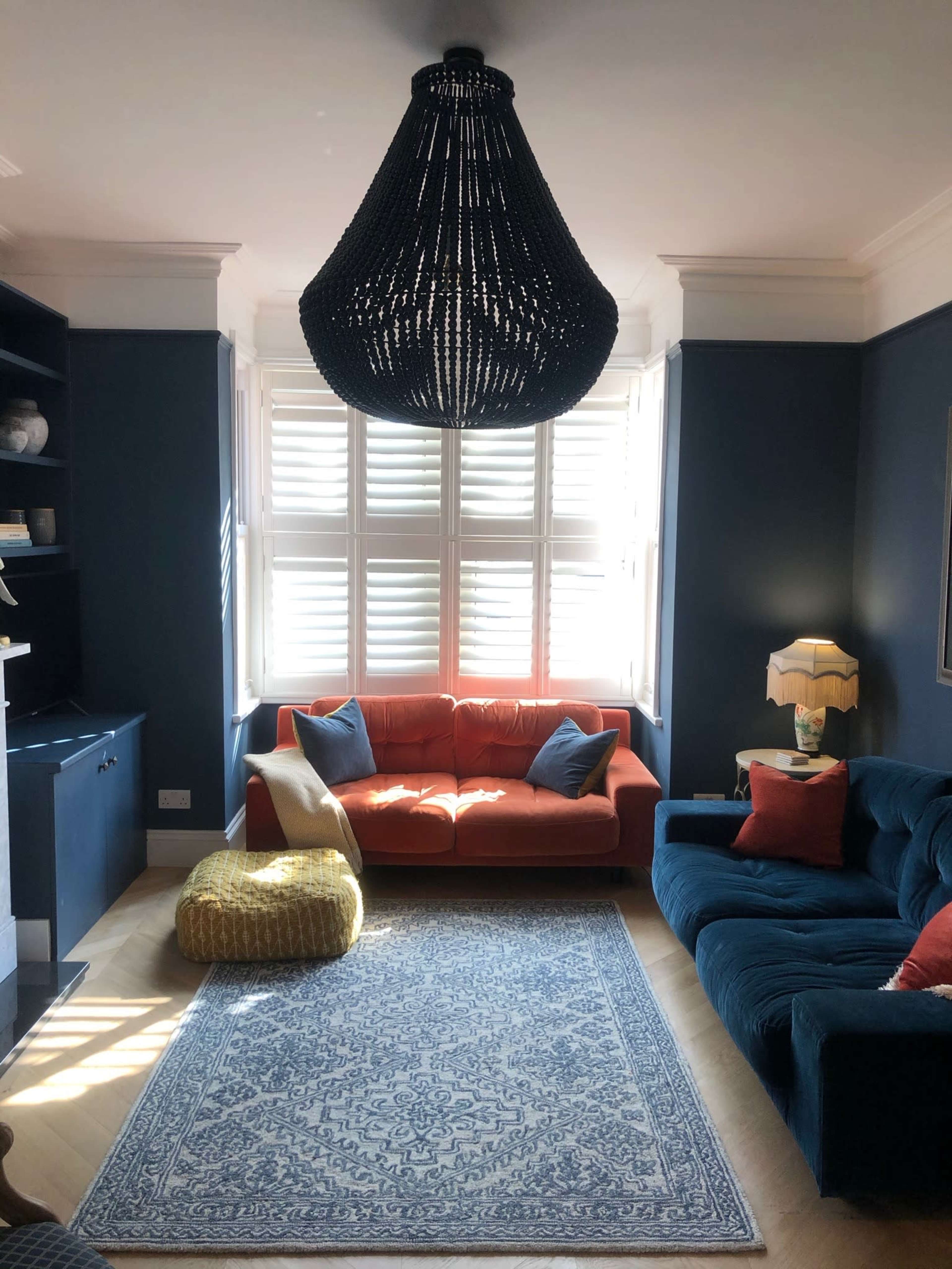 A cozy living room with a blue and orange color scheme, featuring a large woven chandelier, a sectional sofa, a bright orange couch, and a decorative area rug.
