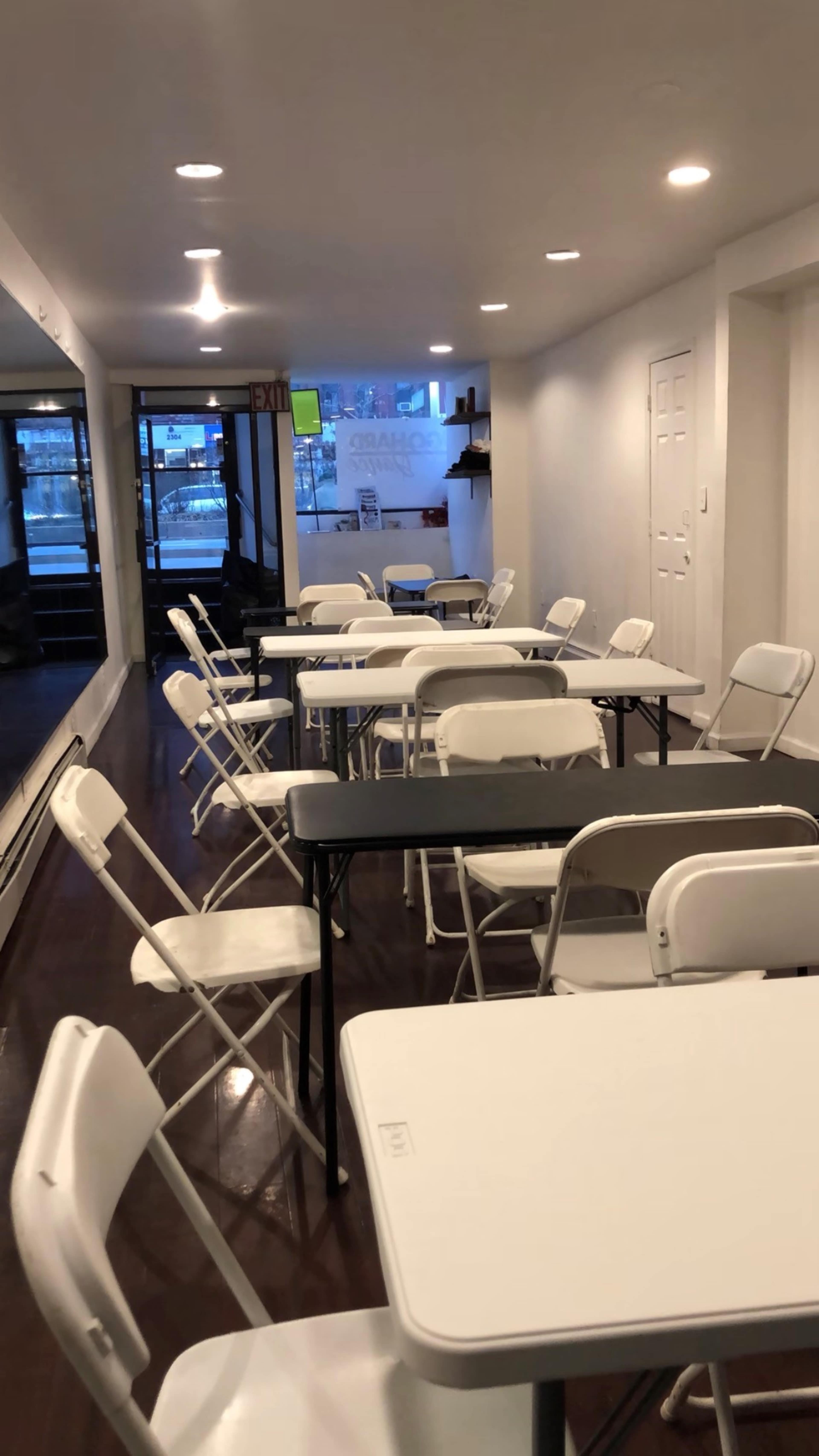 A hallway with several white folding tables and chairs arranged in a sparse manner.