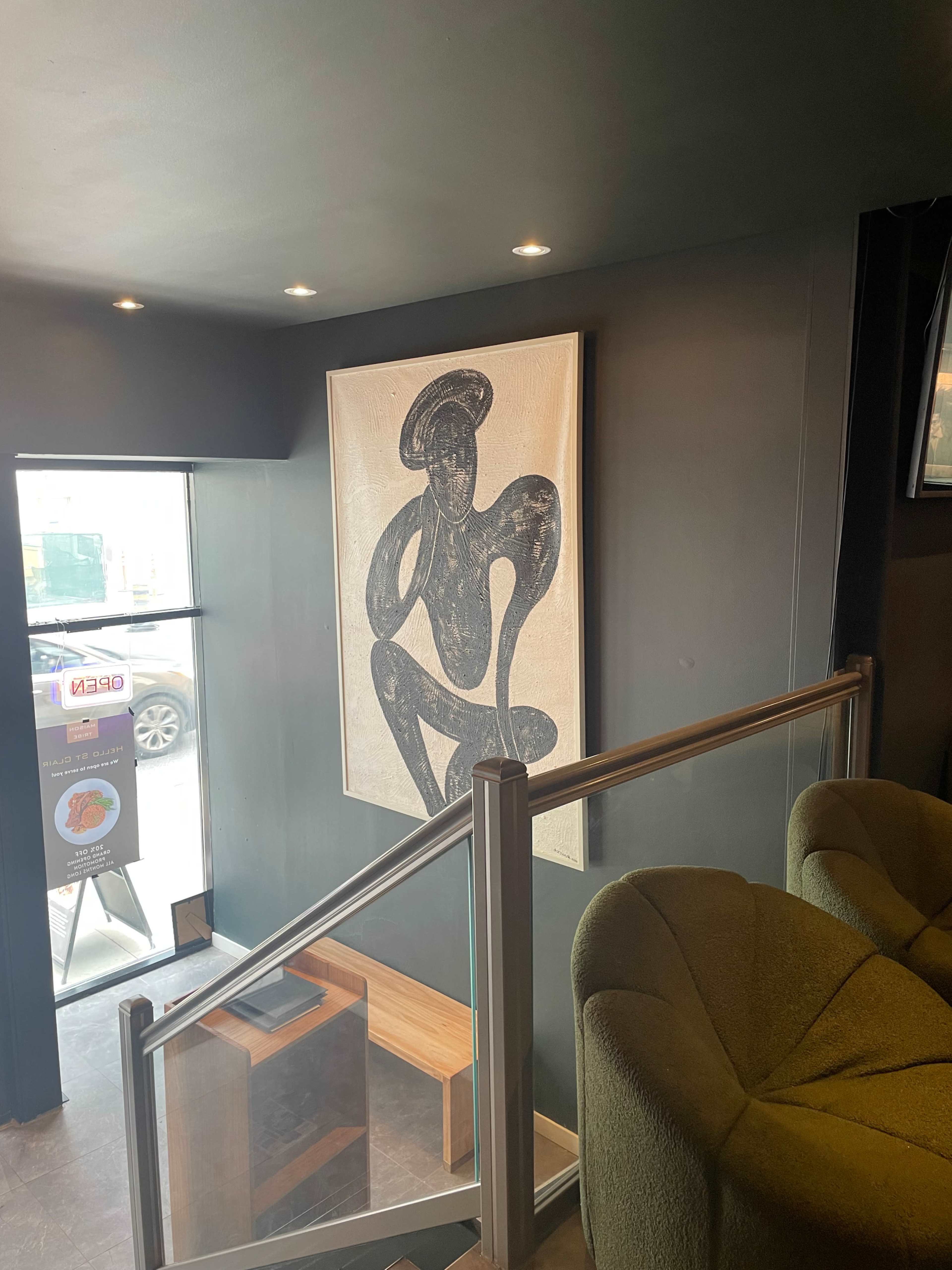 A staircase leading to an upper level, with a large artwork featuring a figure on the wall and a window displaying a street view.