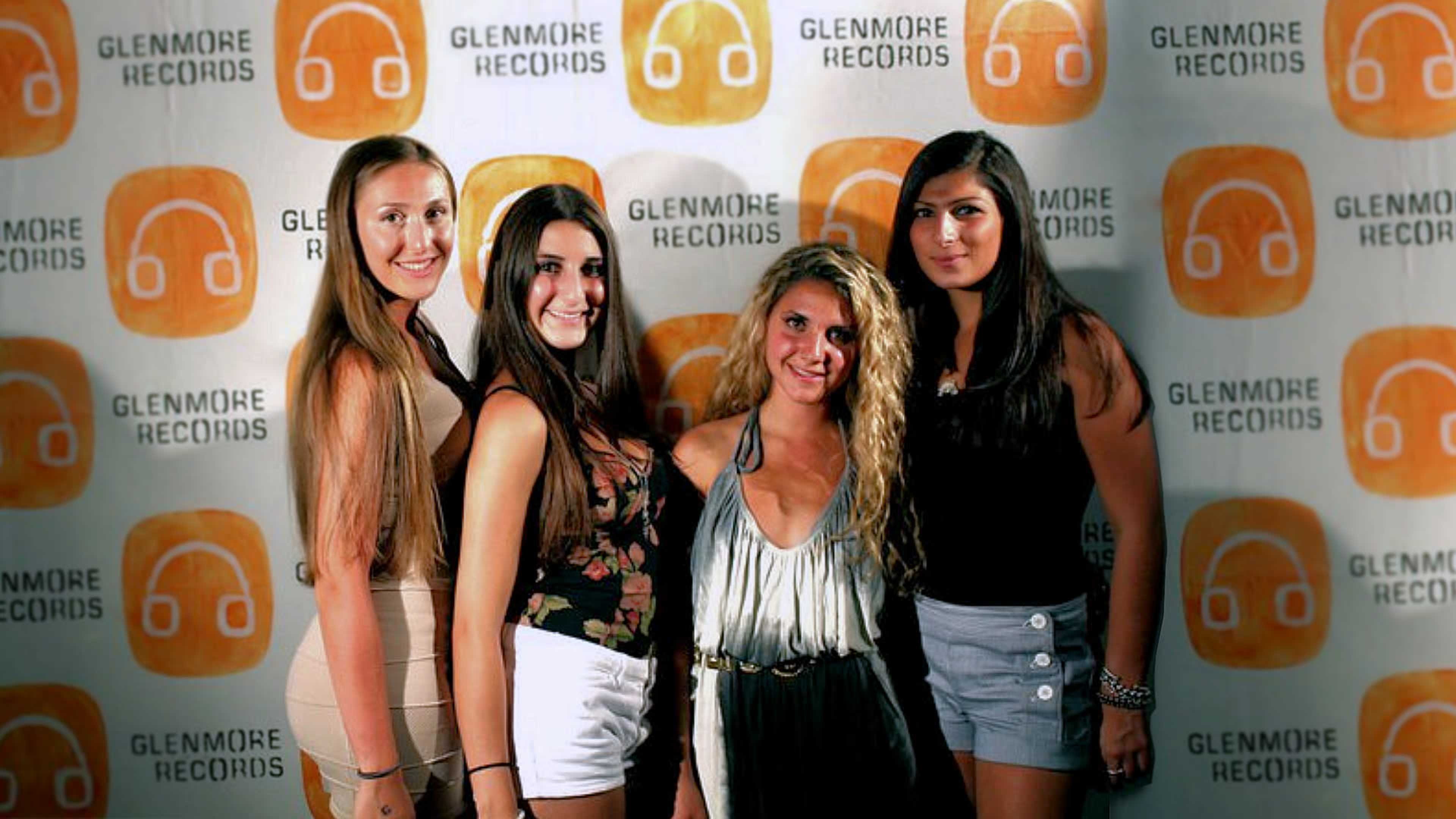 Four women pose together in front of a backdrop featuring the logo of Glenmore Records.