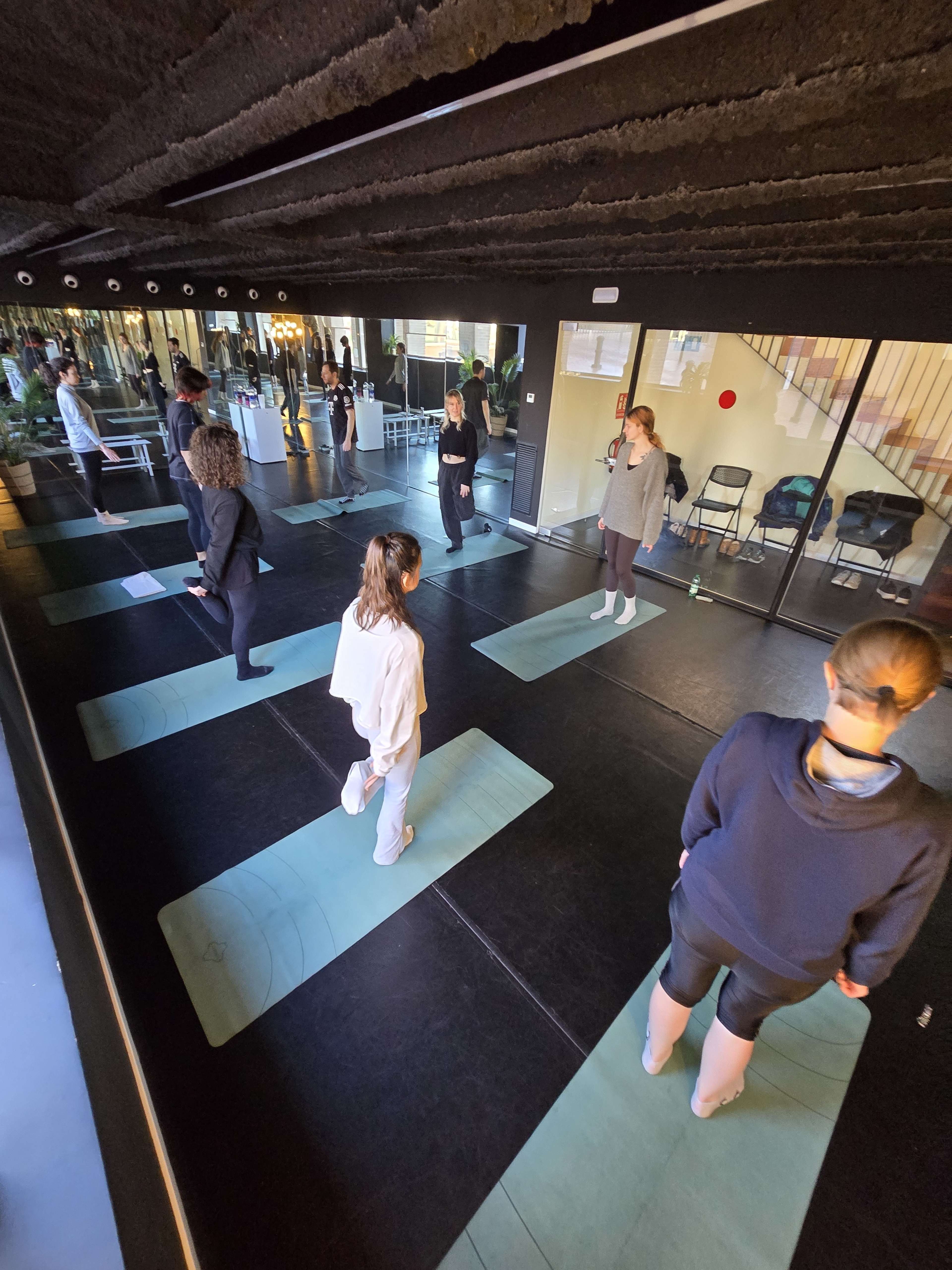 A group of people is practicing yoga on mats in a studio with large mirrors and plants.