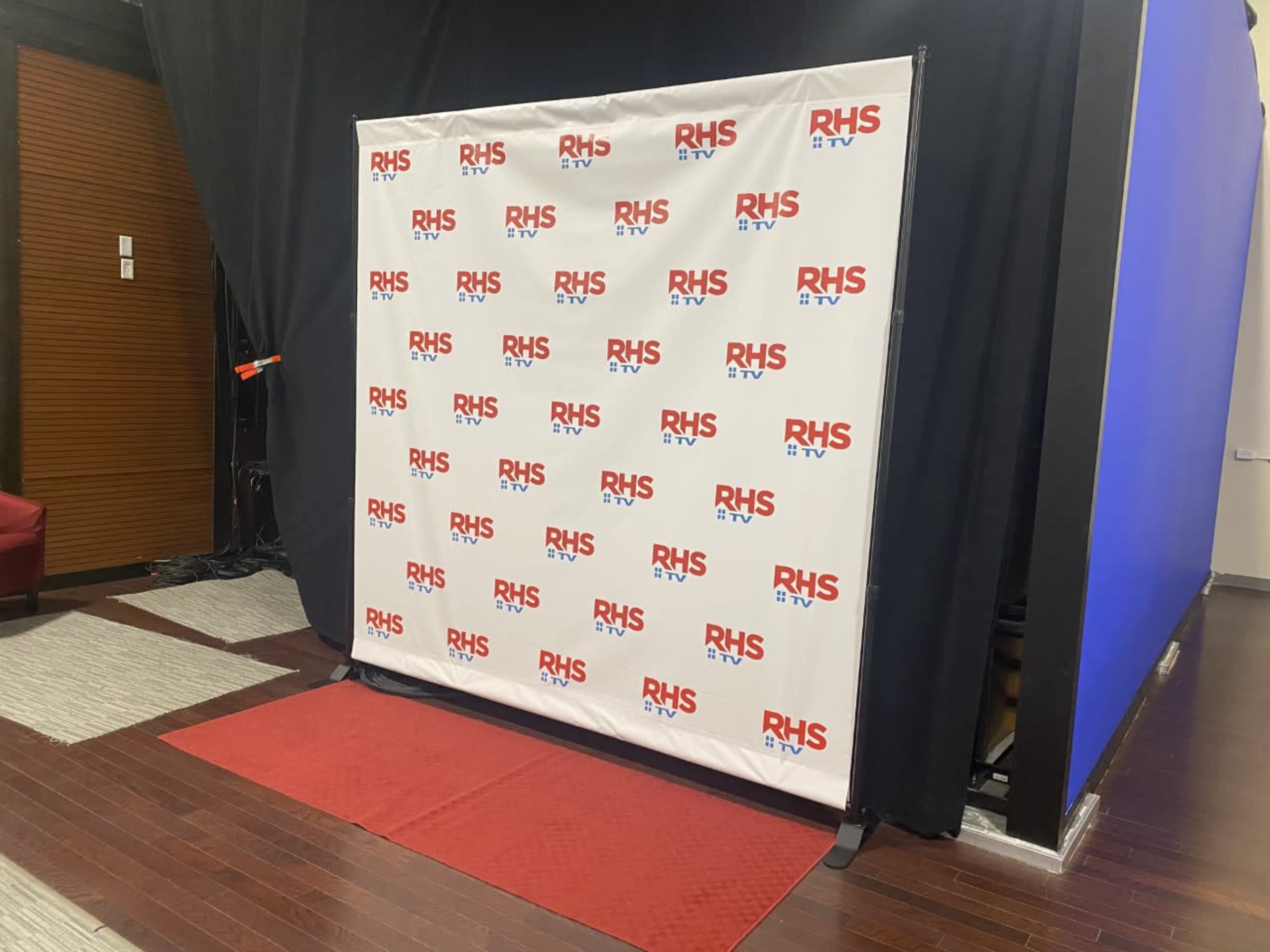 A branded backdrop with "RHS TV" logos set against a dark curtain in a studio environment.
