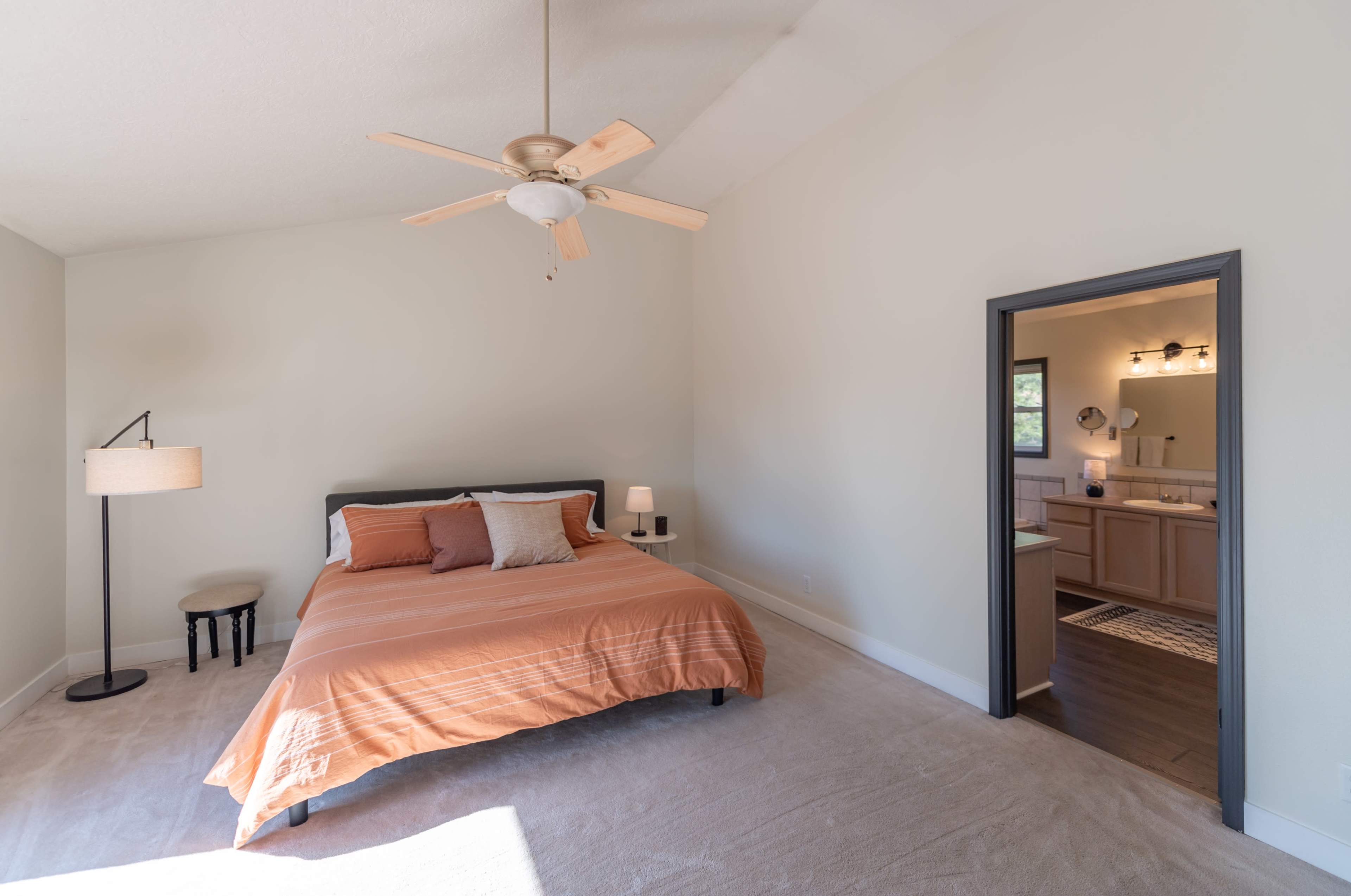 A spacious bedroom with a bed, two lamps, and an open doorway leading to a bathroom.