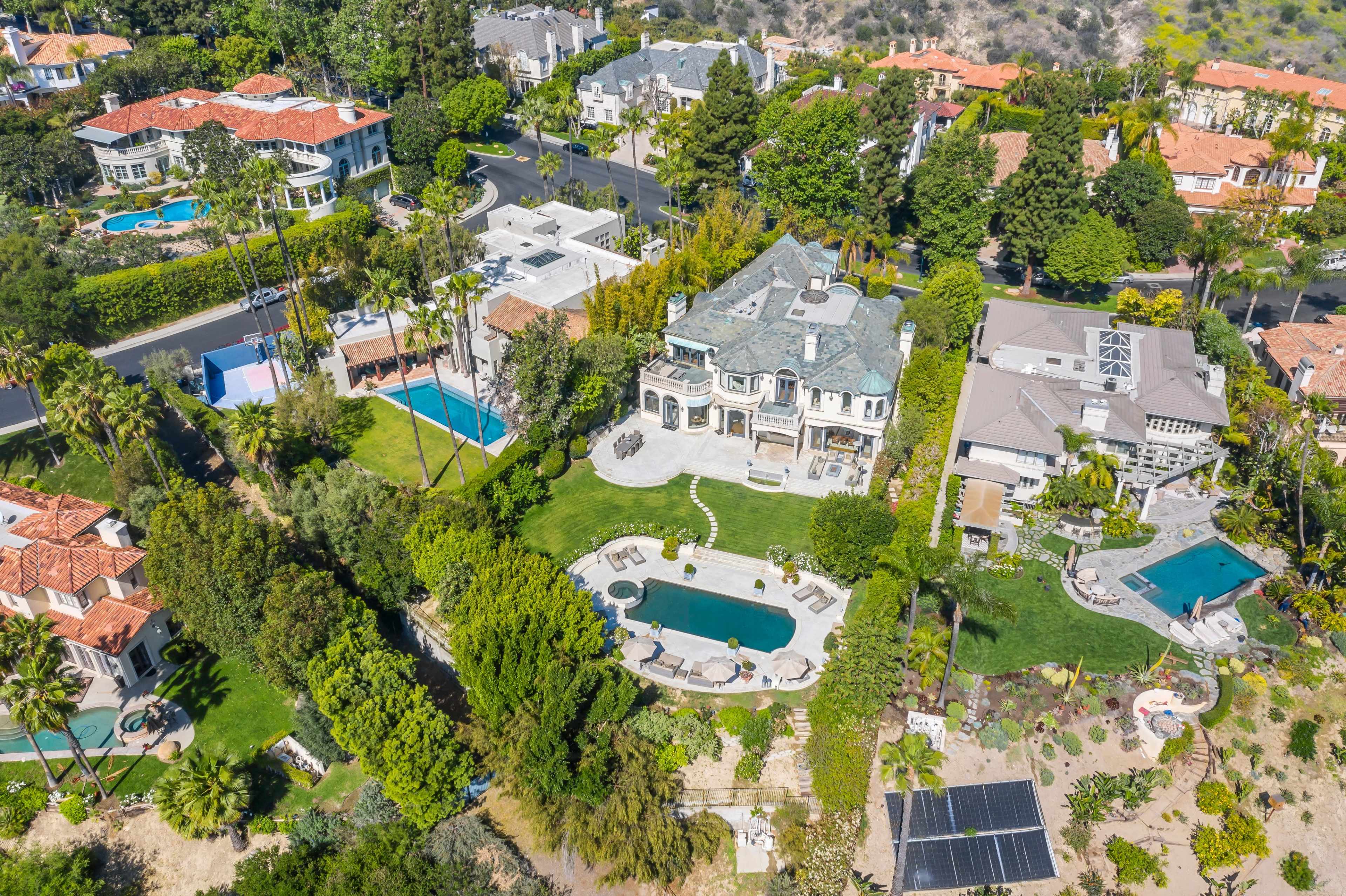 The image shows an aerial view of a residential area featuring large homes with pools, landscaped gardens, and palm trees.