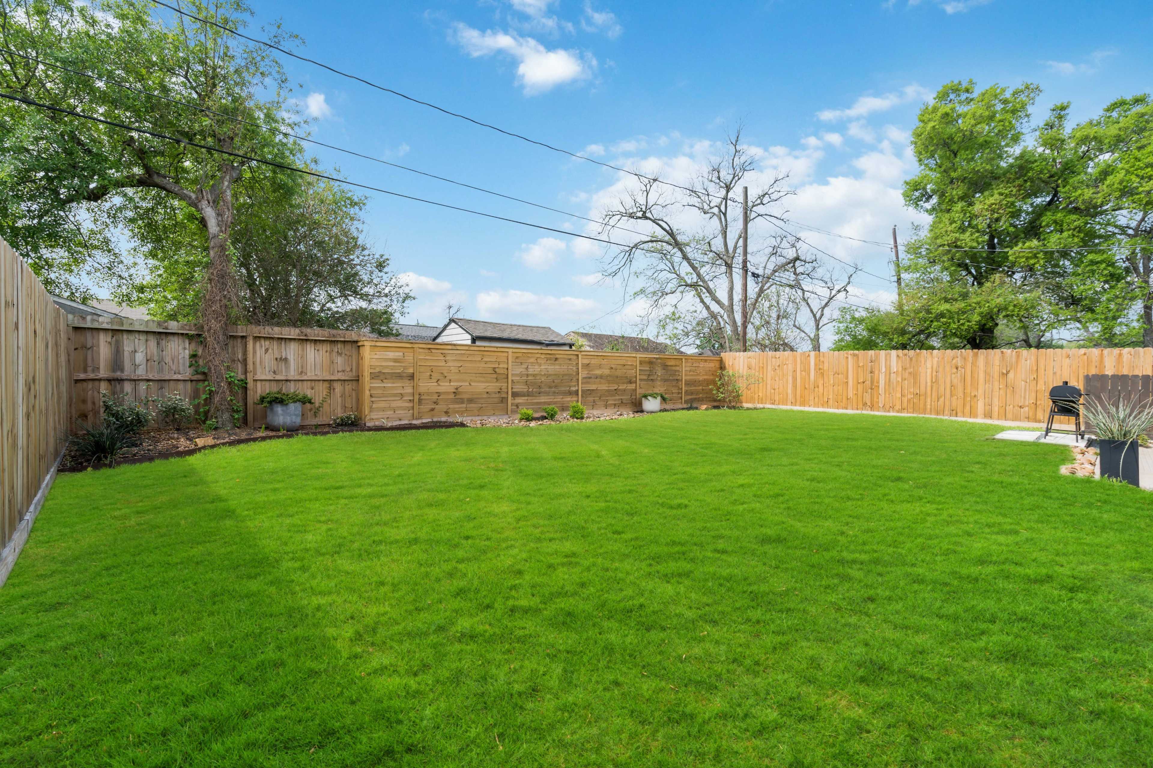 A spacious backyard with a well-maintained grassy area surrounded by wooden fencing.