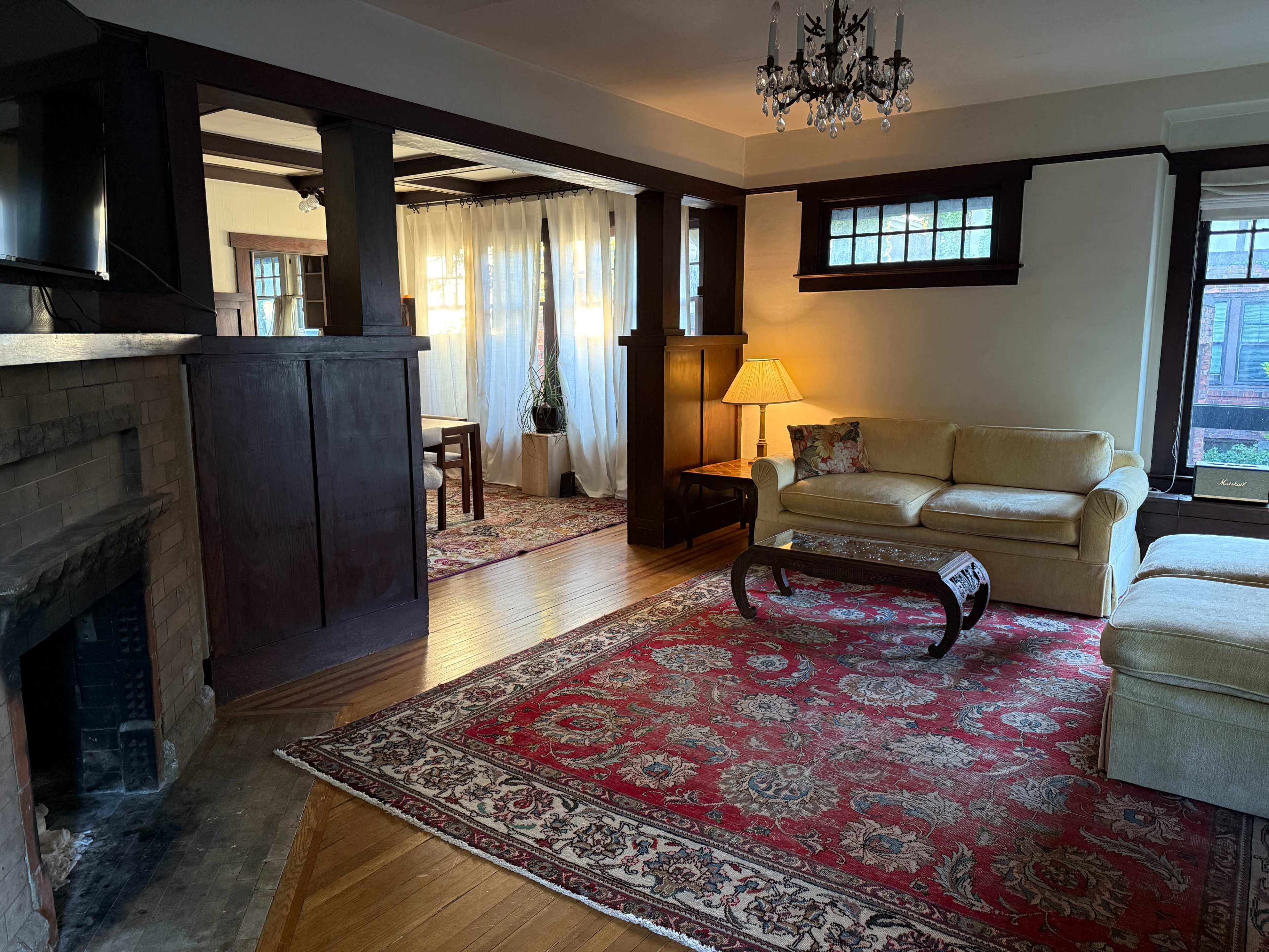 The image shows a living room with wooden paneling, a beige couch, a coffee table, and an ornate area rug, complemented by a lamp and a fireplace.