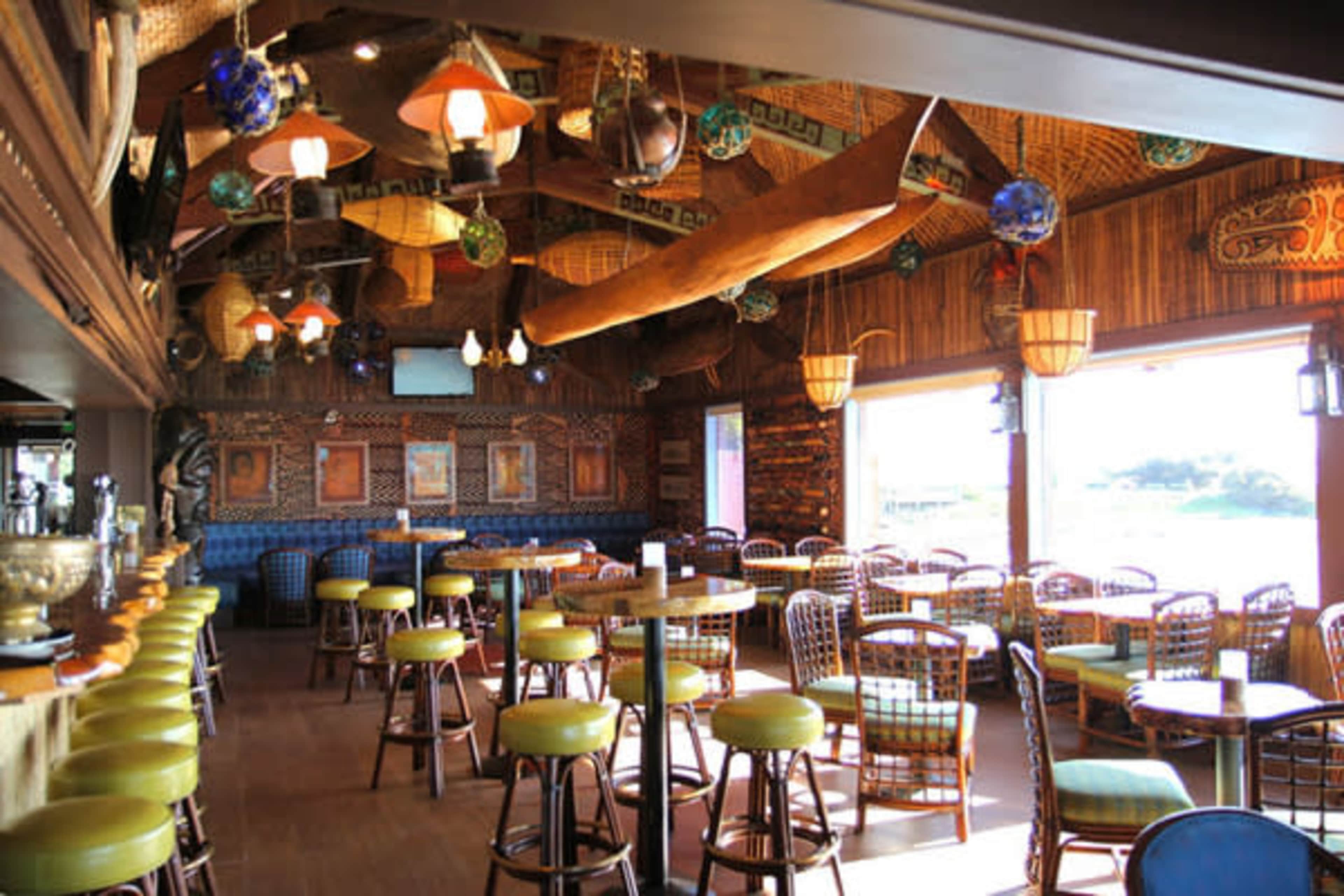 The image shows a brightly lit interior of a restaurant featuring wooden furniture, woven decorations, and vibrant hanging lights.