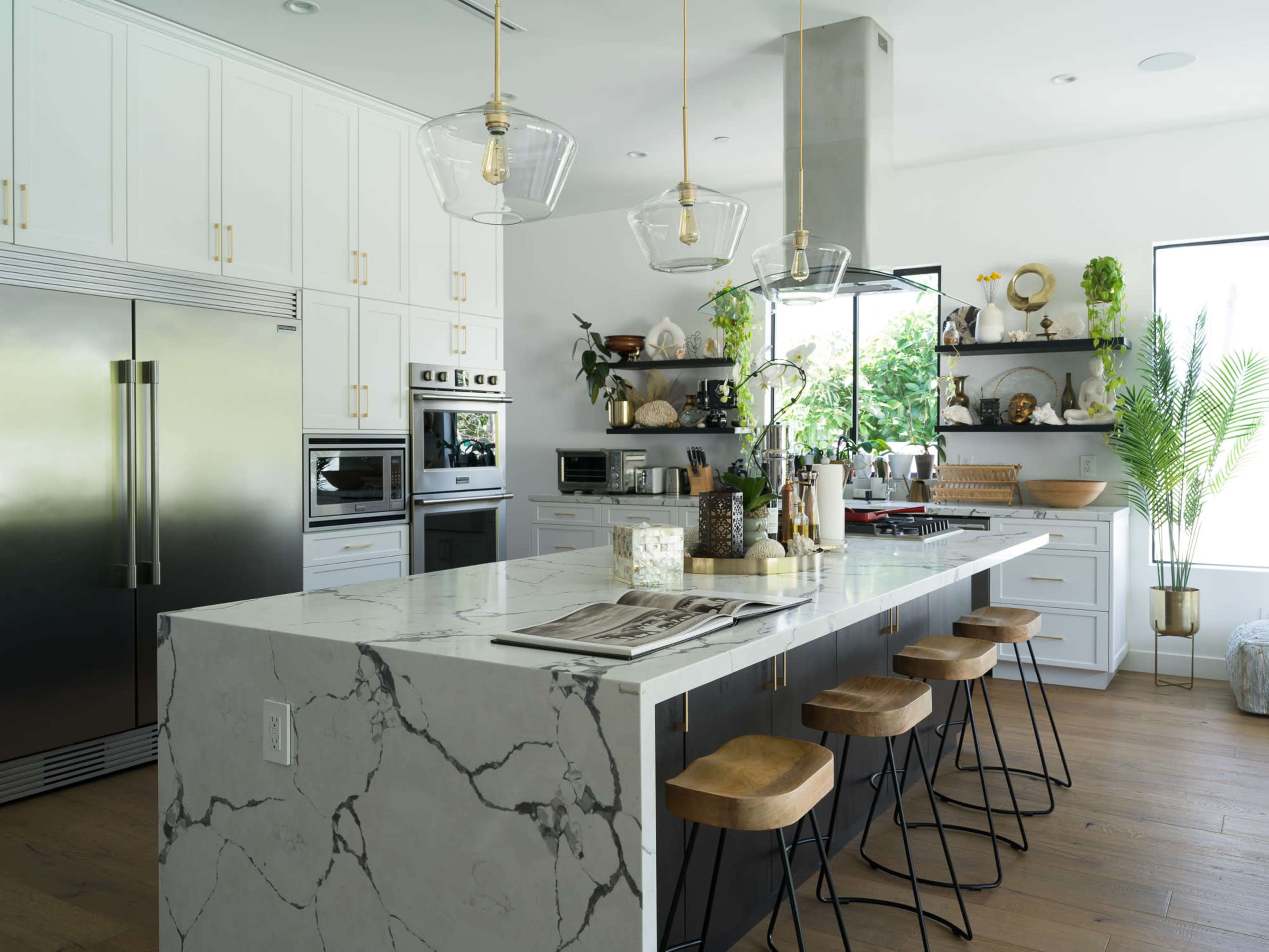 The kitchen features white cabinetry, stainless steel appliances, and a large marble countertop with wooden bar stools.