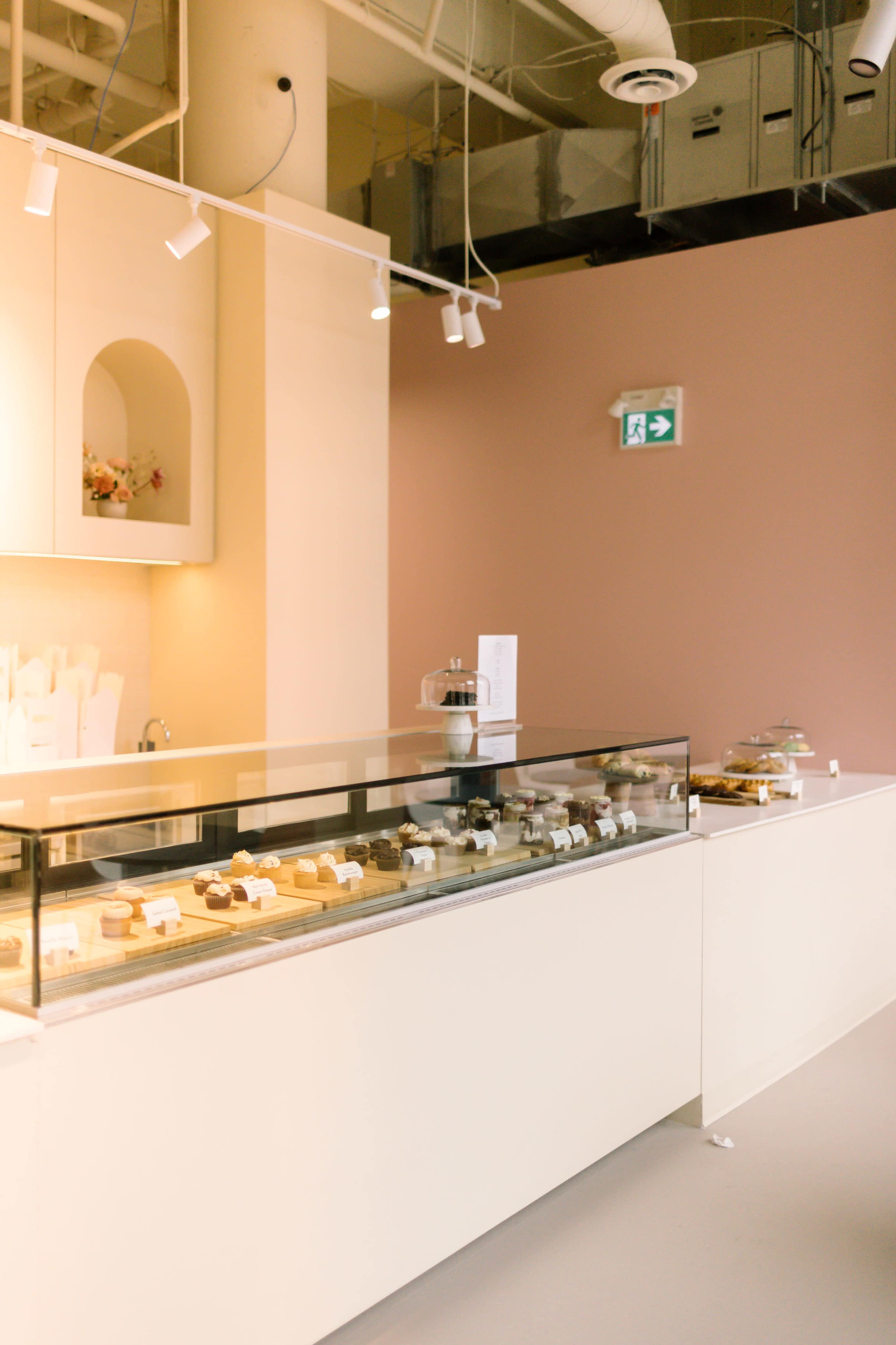 A light-toned dessert display case in a modern bakery, featuring a variety of pastries and cakes under glass.