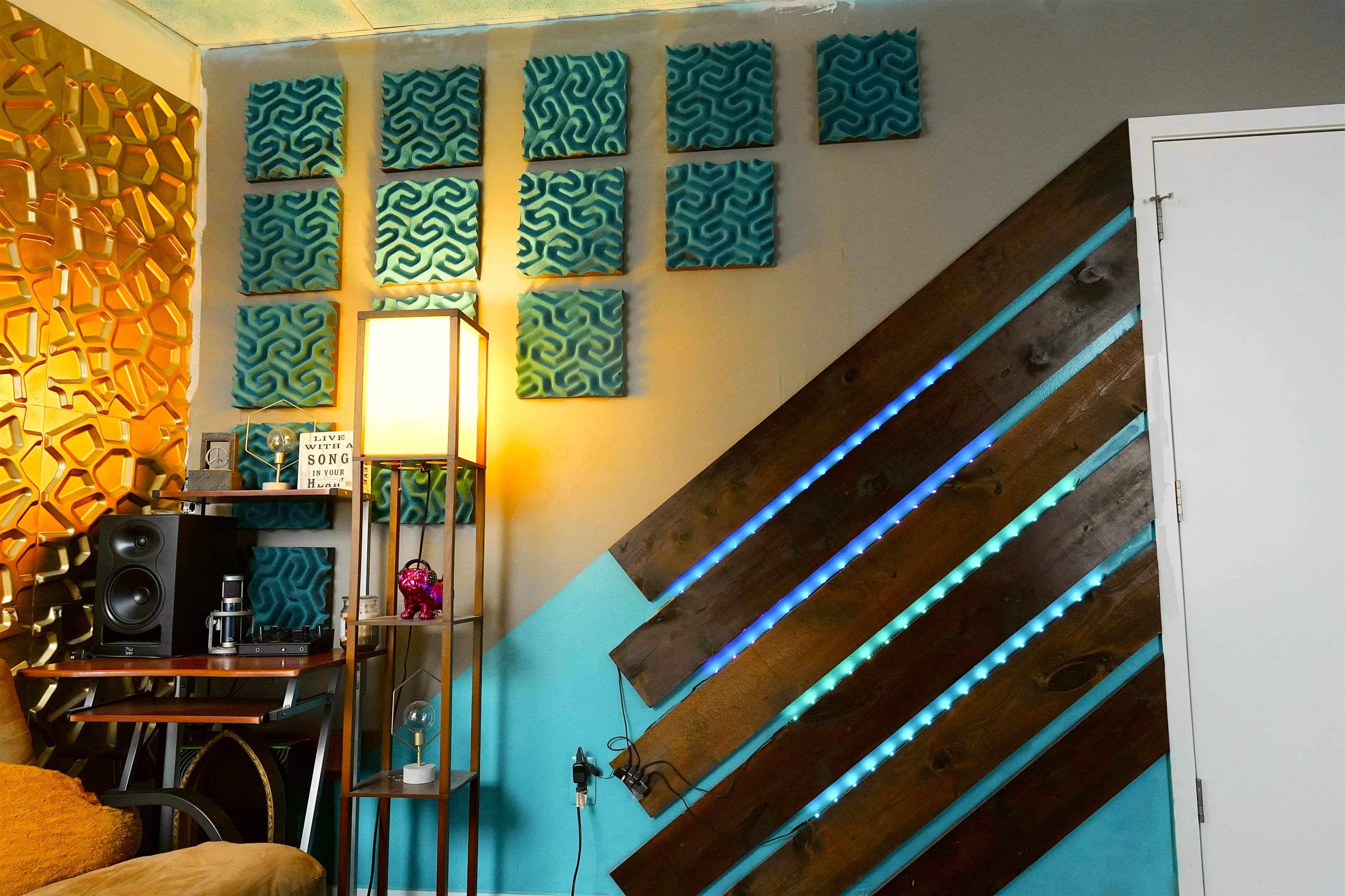 The image shows a cozy room with a decorative wall featuring acoustic panels, a lamp, a speaker system, and a wooden wall accent with LED lights.