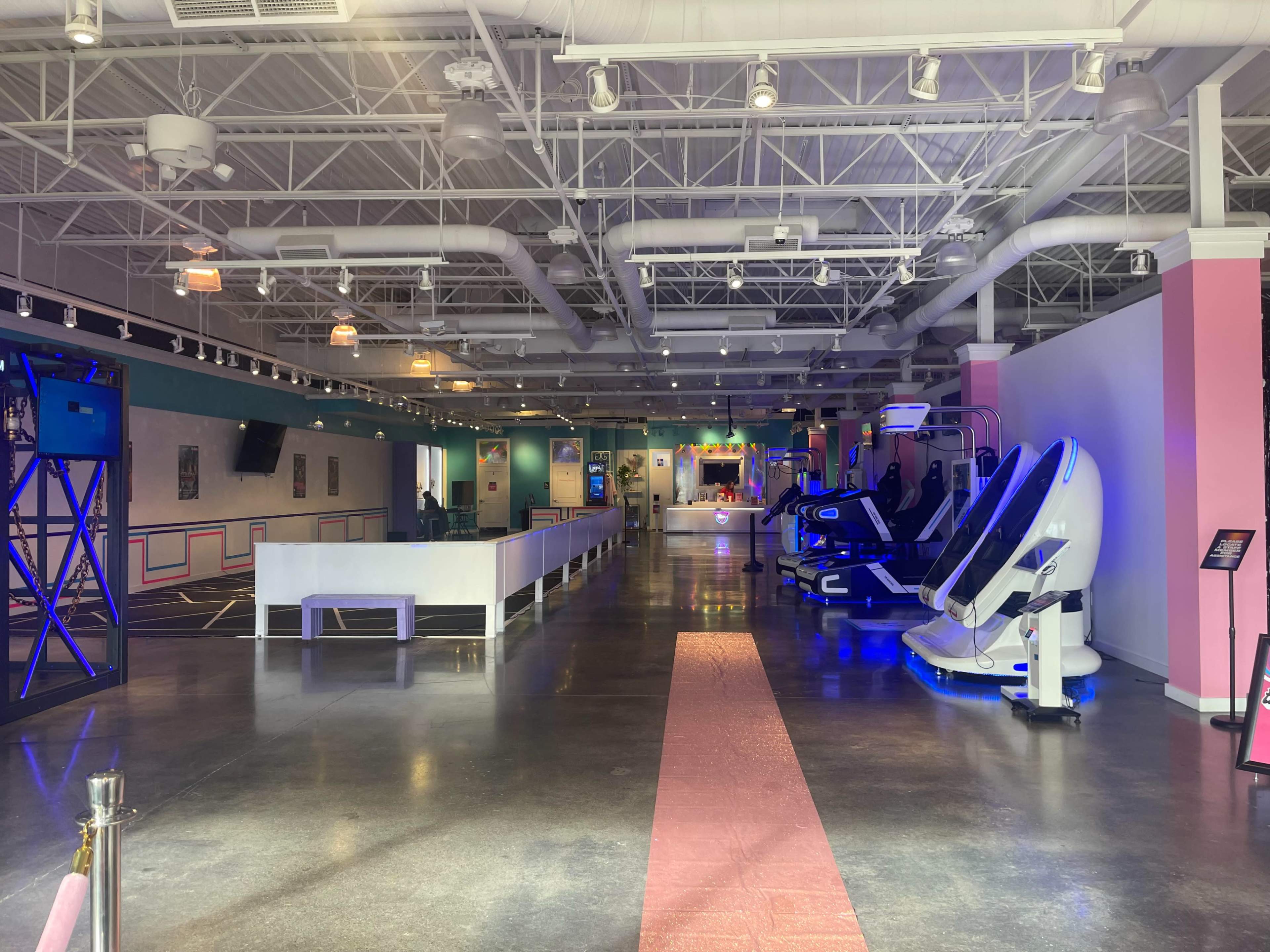 A spacious, brightly lit entertainment facility with various exercise equipment and sleek booths arranged along the walls.