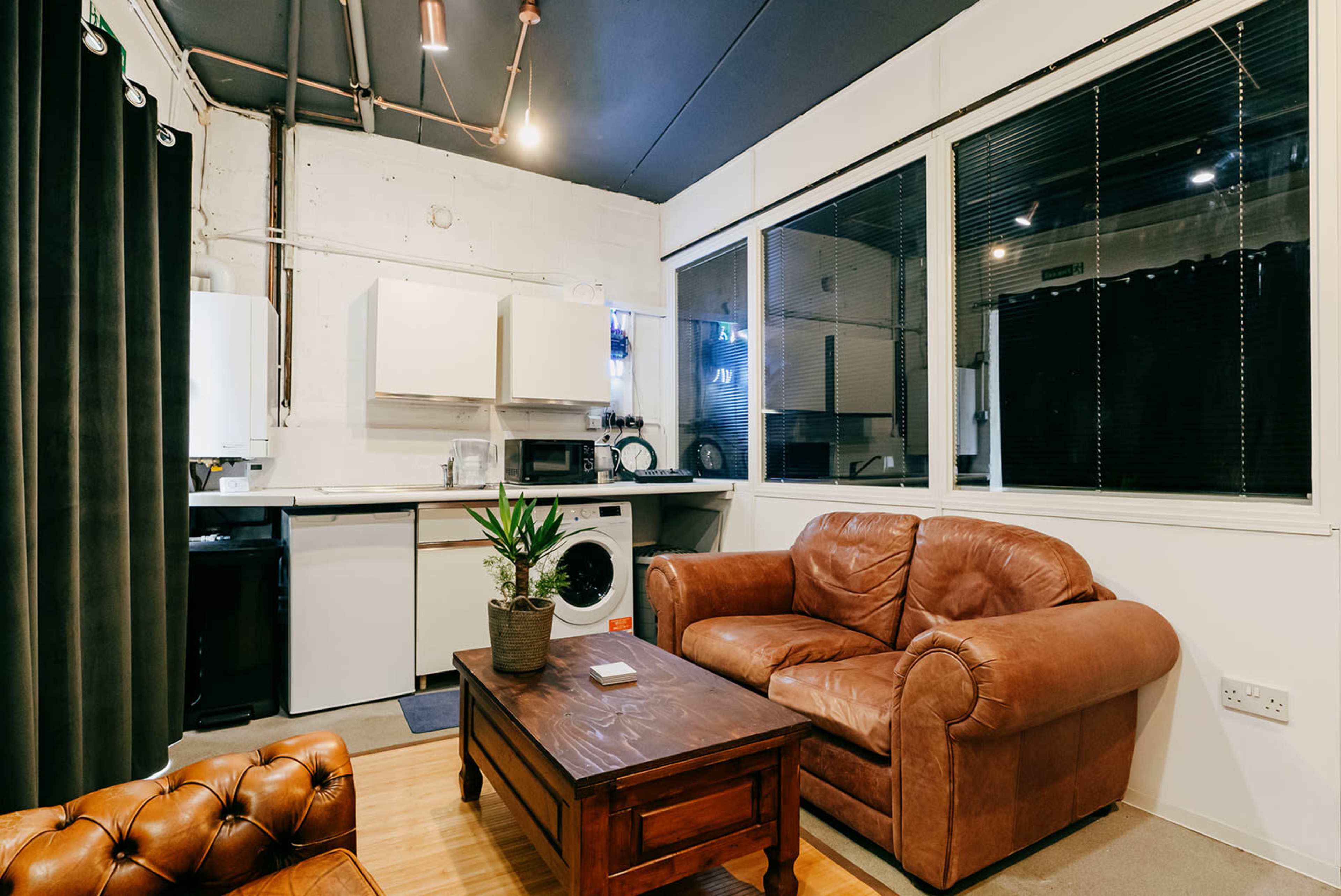 A cozy living area with a brown leather sofa, a wooden coffee table, and a kitchenette featuring white cabinets and various appliances.