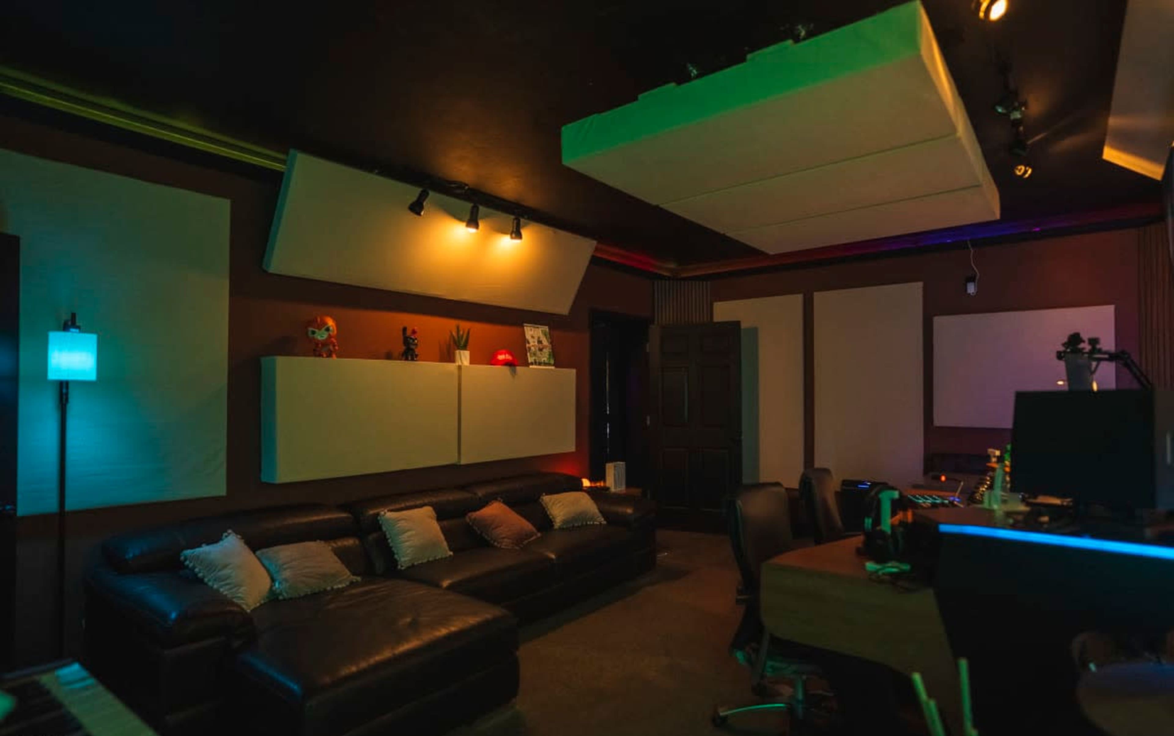The image shows a dimly lit music studio with a black leather sofa, soundproof panels on the walls, and various artistic decorations on display.